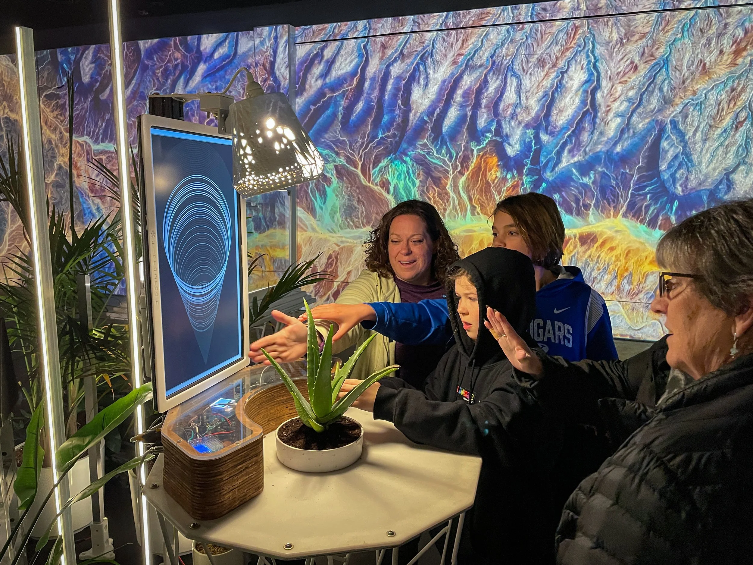 JUMP ILLUMIBRATE 2024 immersive room, guests reaching toward an interactive station beneath projected terrain from space