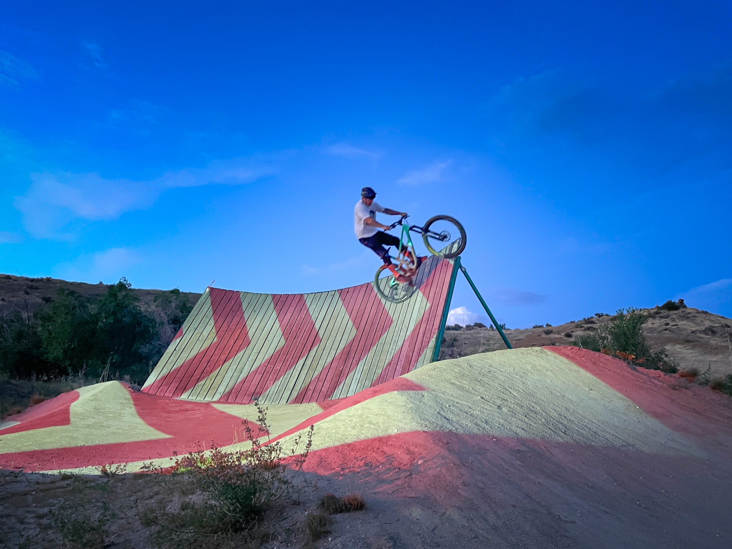Rider crests a chevron mapped wooden wall ride at Boise Bike Park, front wheel lifting over the lip at dusk.