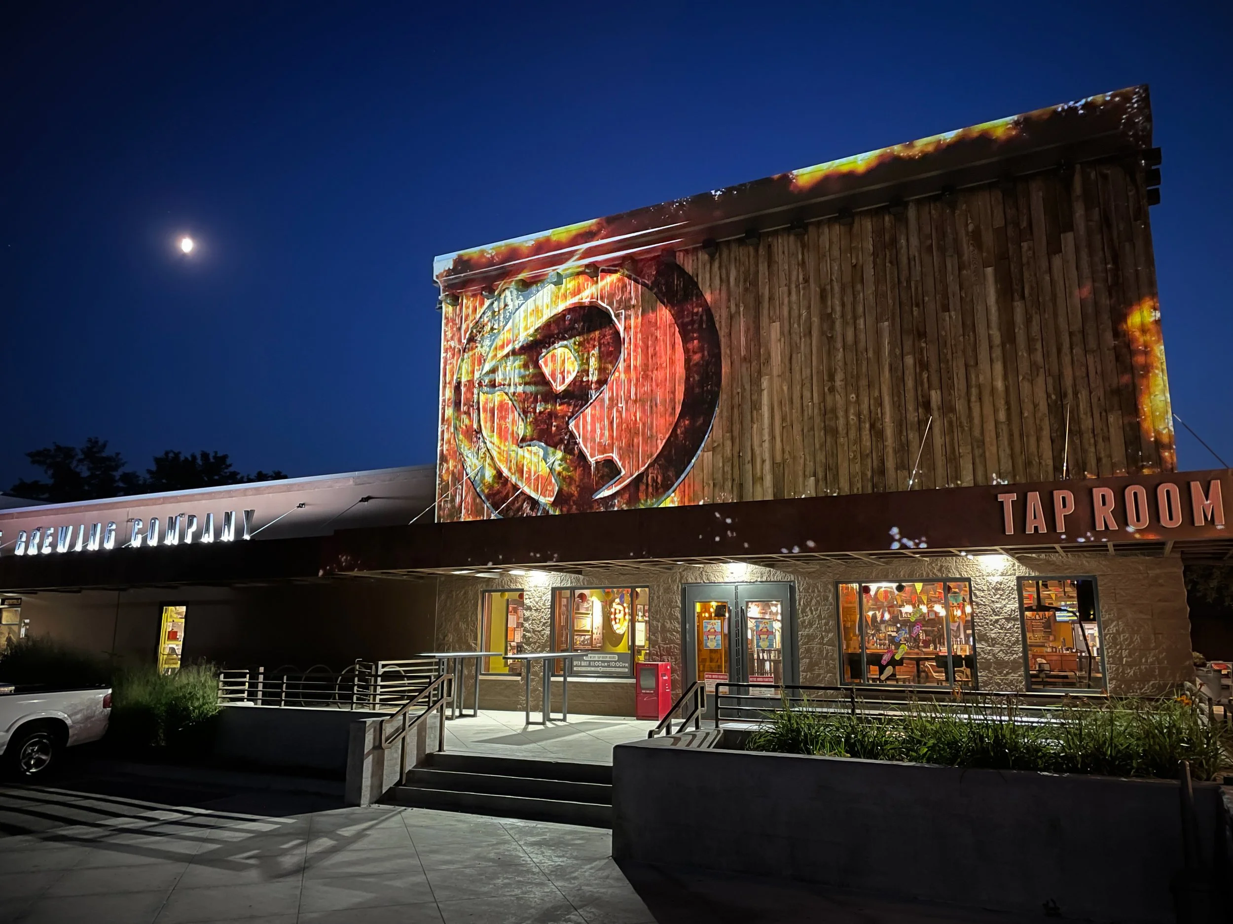 Payette Brewing facade in Boise lit by projection mapping at night, moon visible at left.