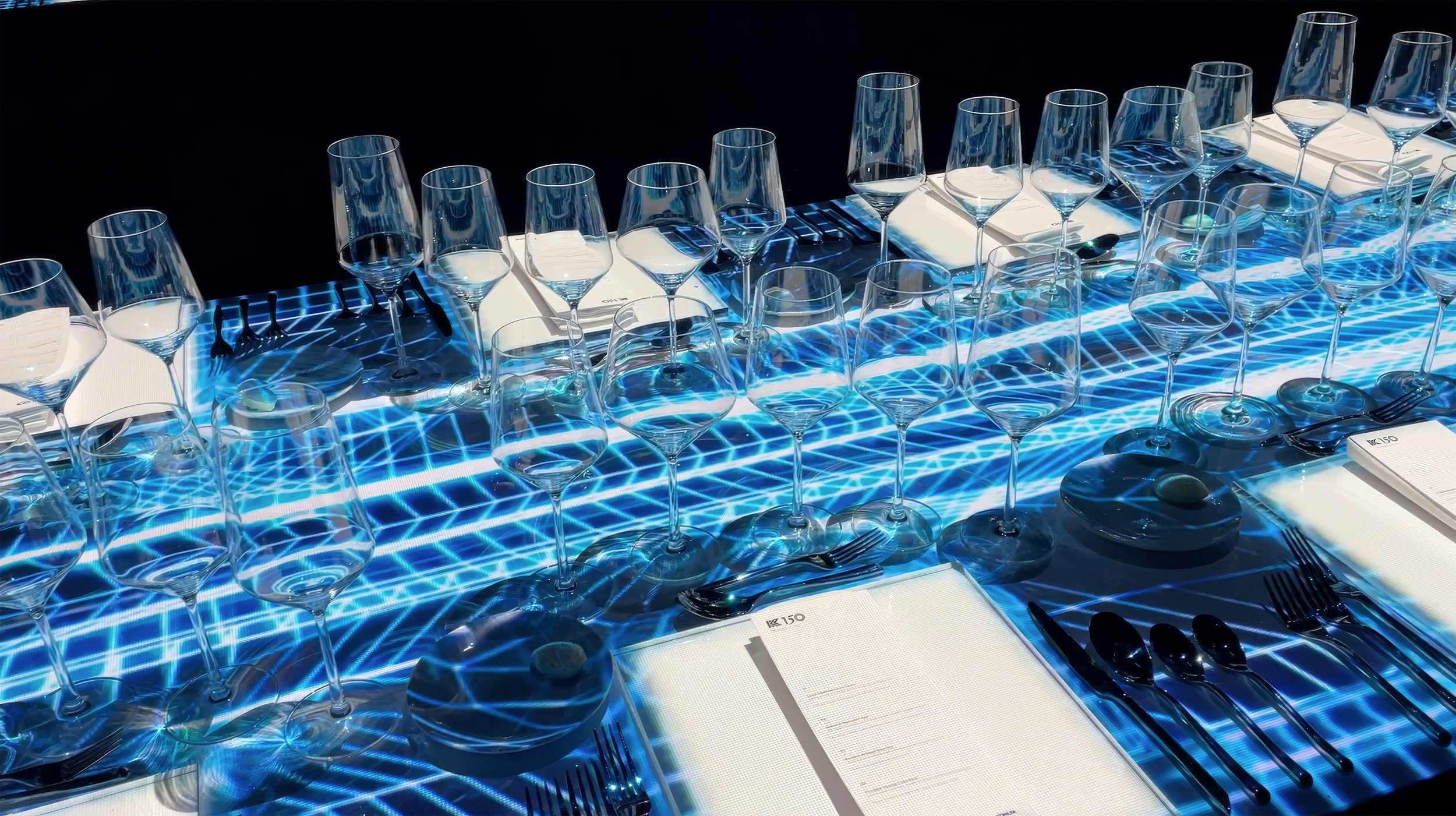 Kohler K150 immersive dining projection mapping, blue wireframe visuals refracting through clear glassware