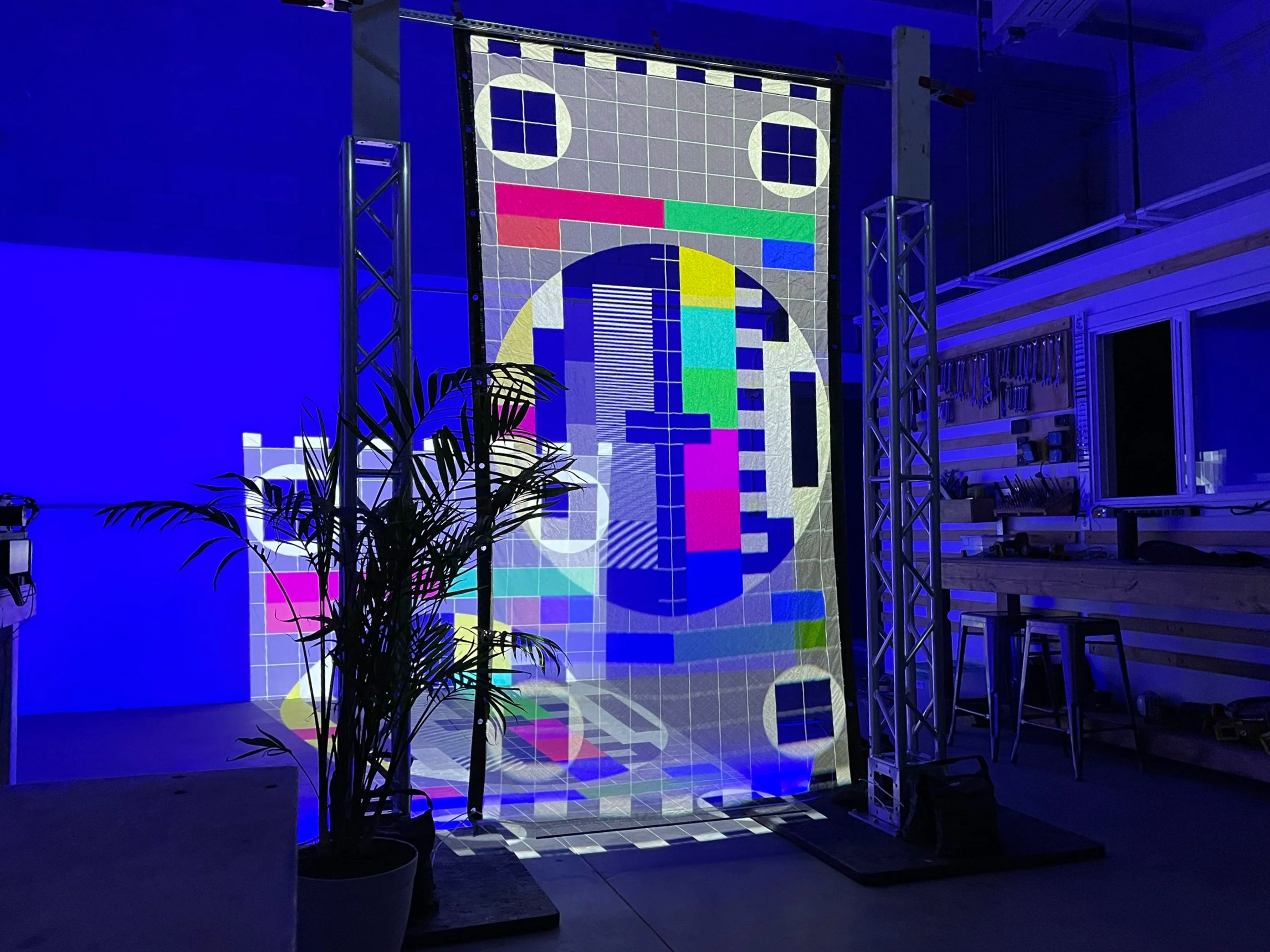 Color test pattern projected on a vertical hologram scrim in a blue lit studio, spill spreading across wall and floor