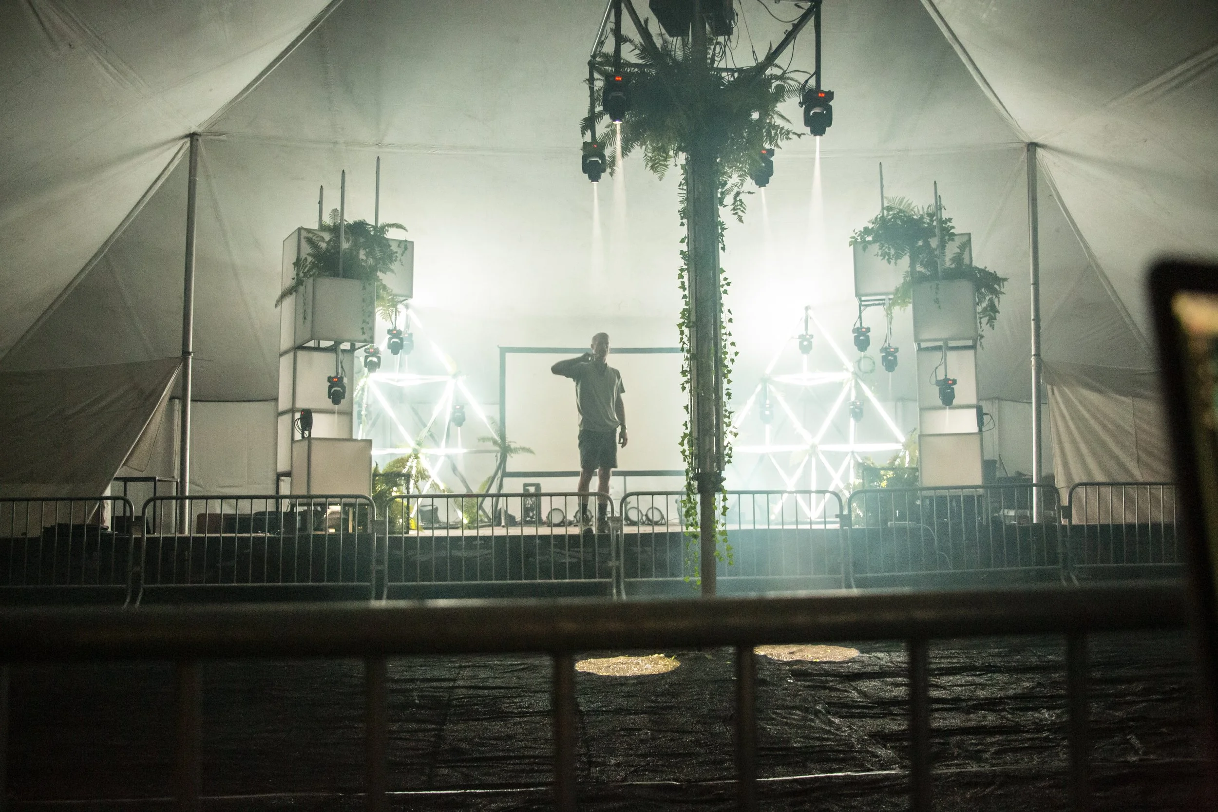 Lighting design stage build in a tent, lit triangle trusses and moving heads framing a load in checkpoint