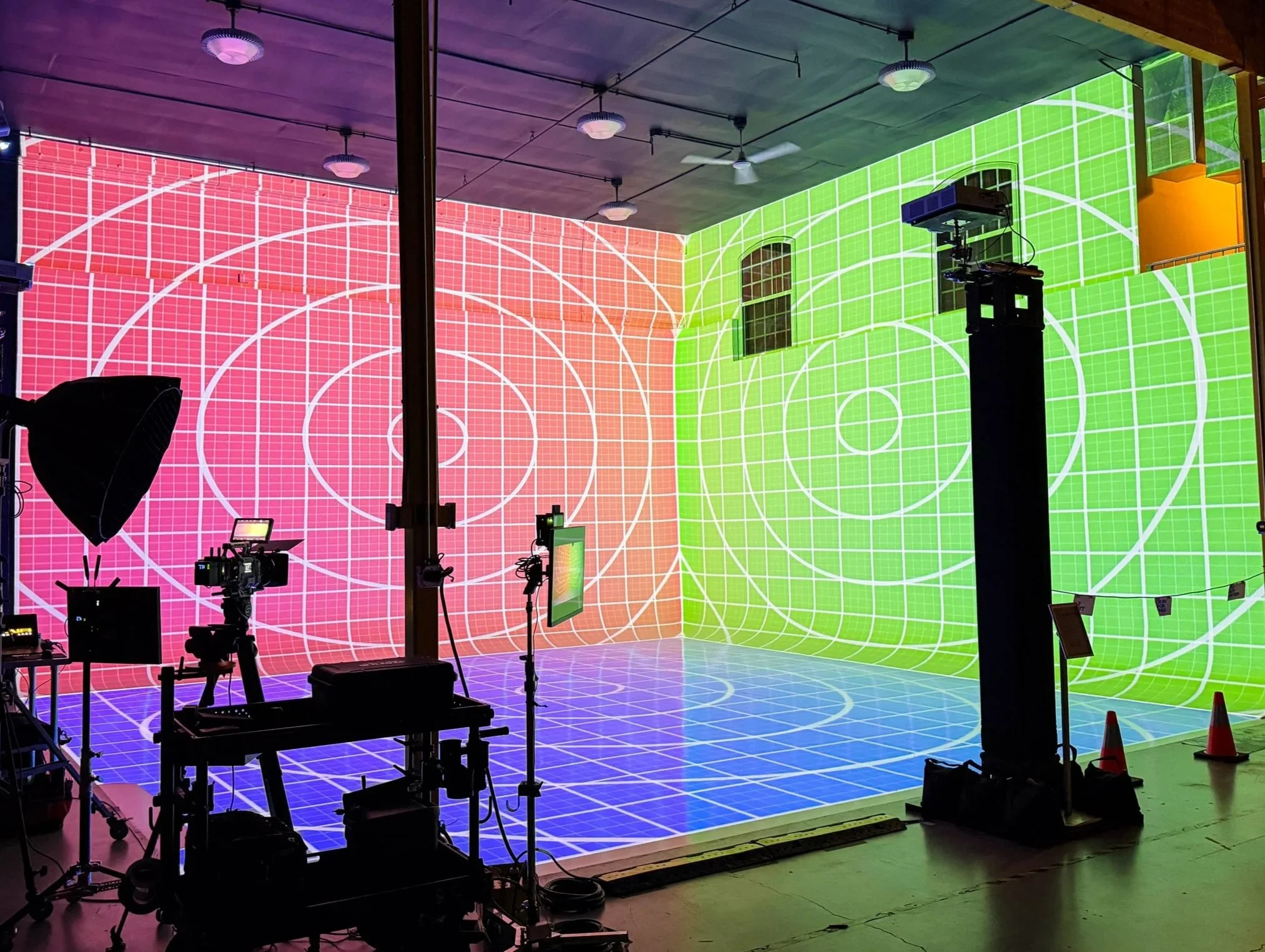 Immersive projection mapping room mid calibration in a pink to green gradient grid, projectors and camera rig staged inside