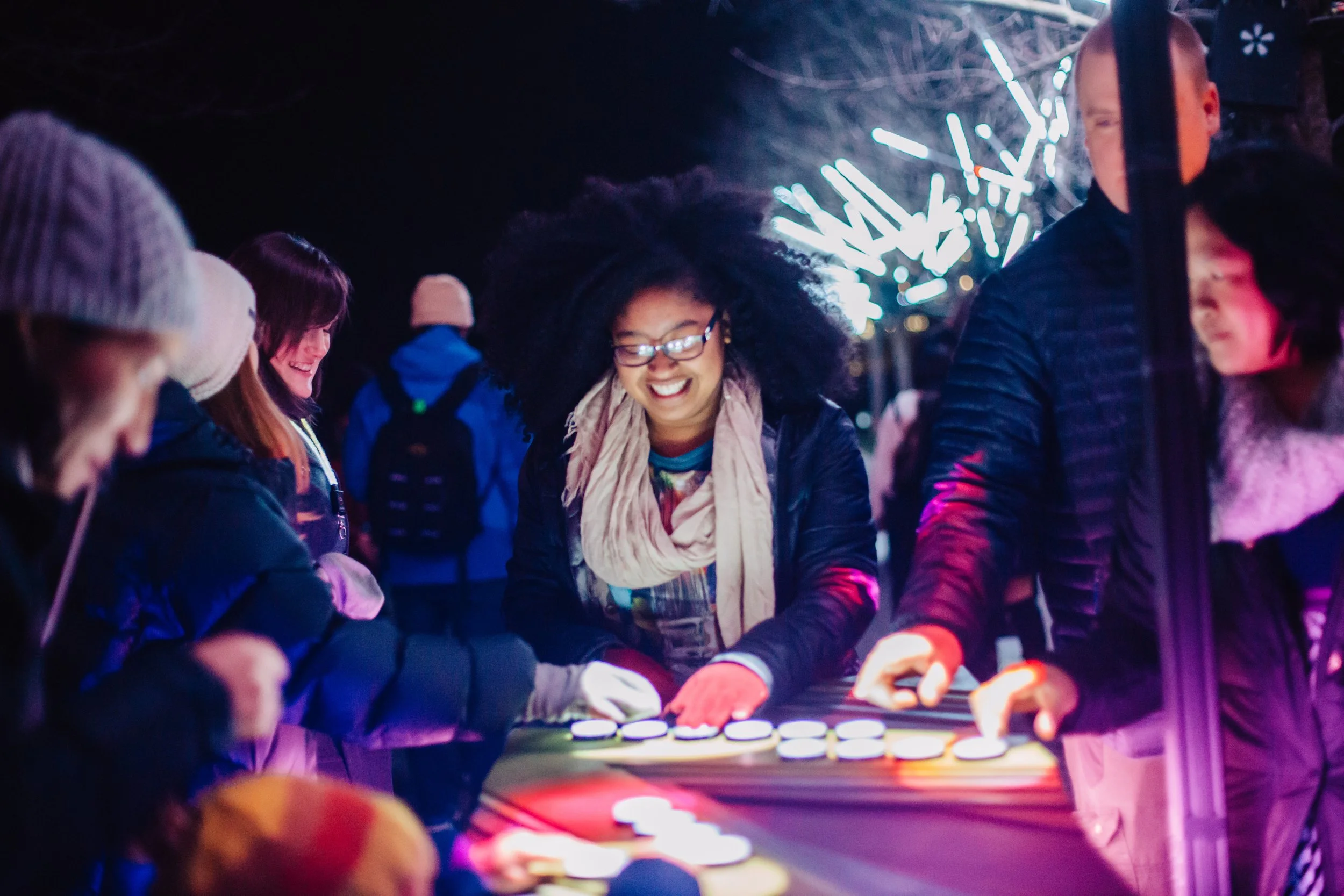 Interactive light table at an outdoor night festival, guests smiling as their drawings appear in the air above