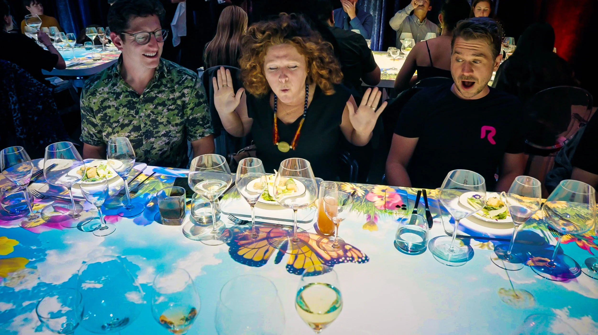 Projection dining by NOVA Light Labs, guests reacting to a sky and butterfly scene mapped across the table.