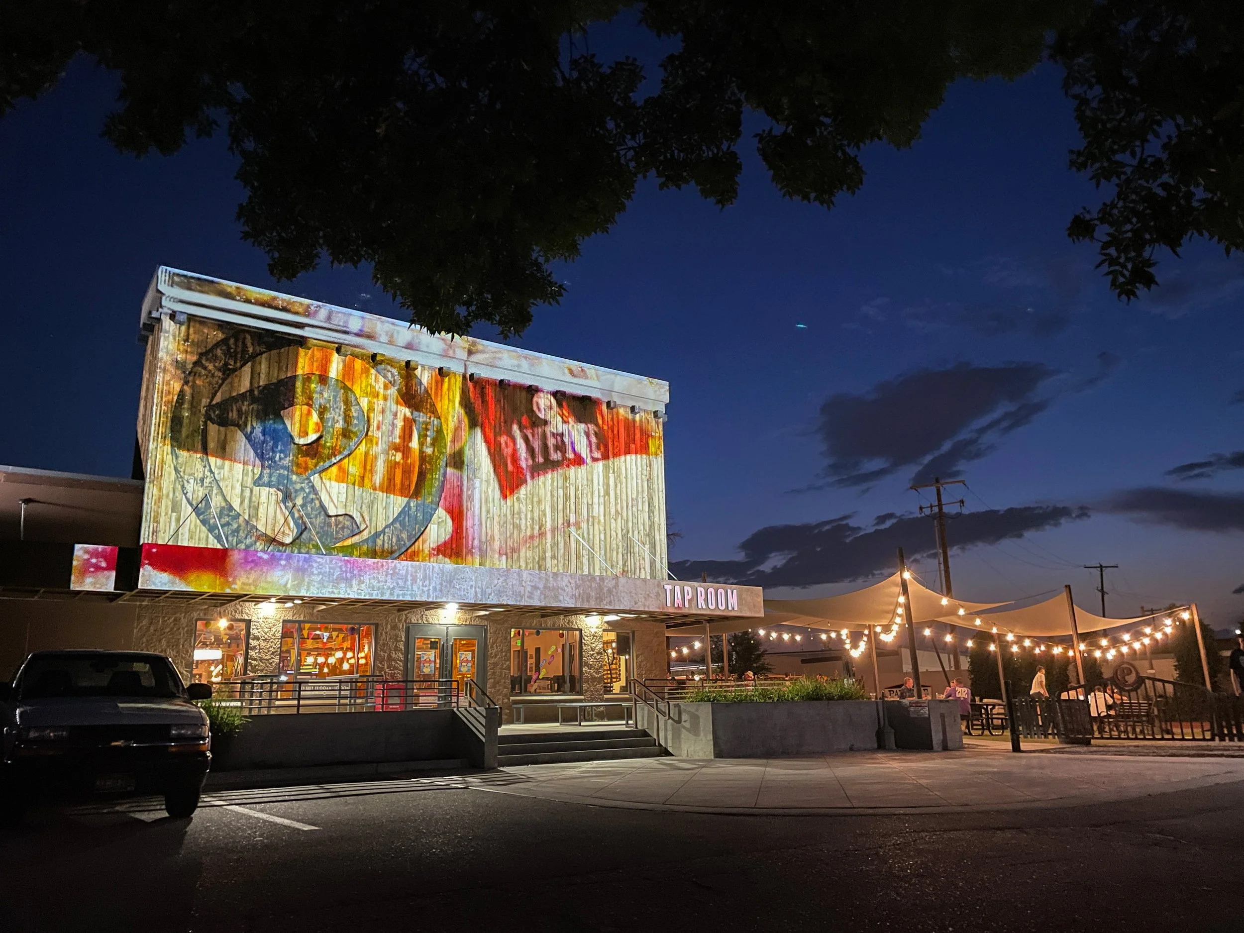 Projection mapped Payette Brewing taproom facade in Boise at dusk, patio string lights glowing at right.