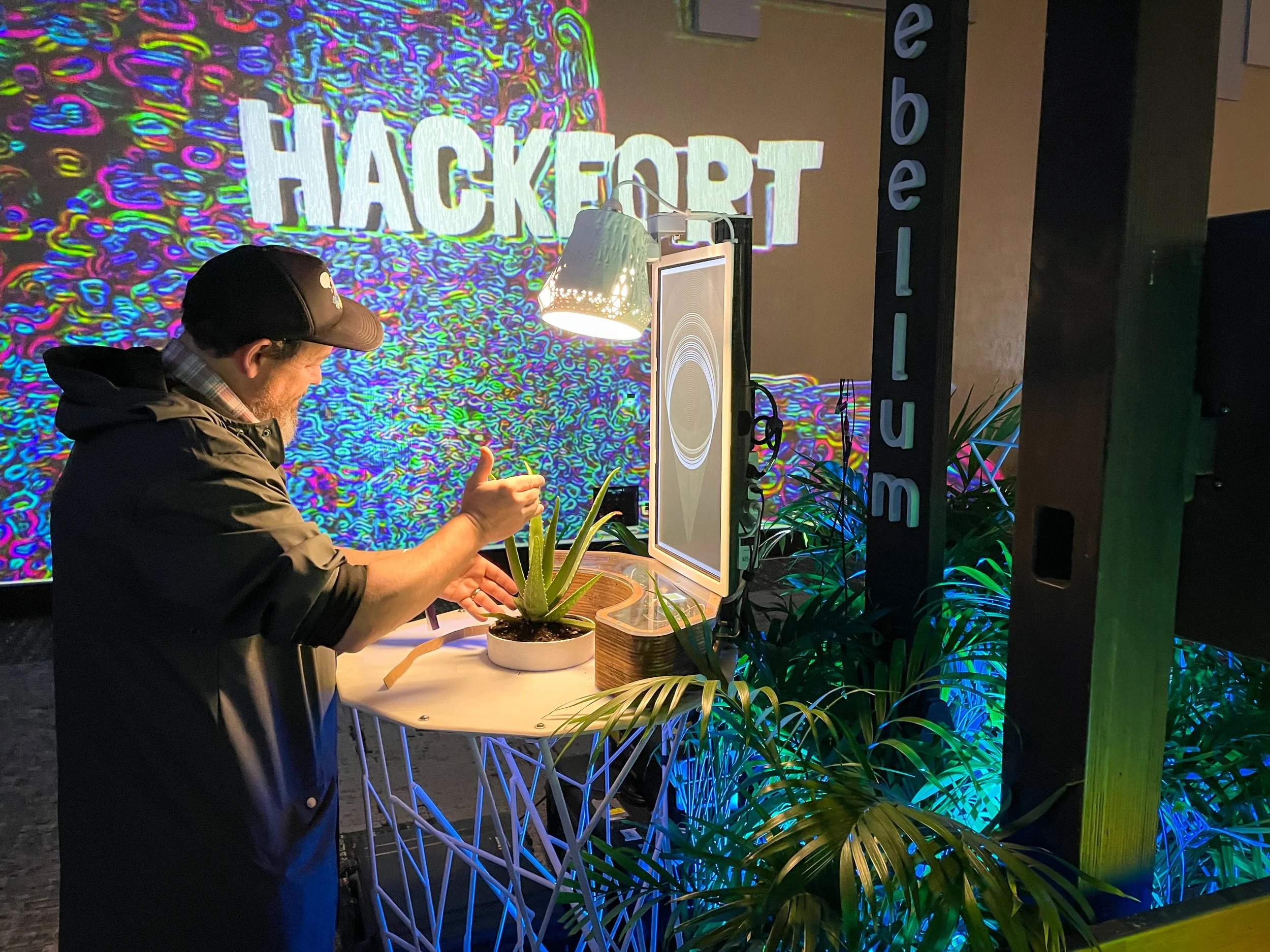 Guest gestures at a screen based video feedback station at Hackfort, colorful feedback filling the wall behind
