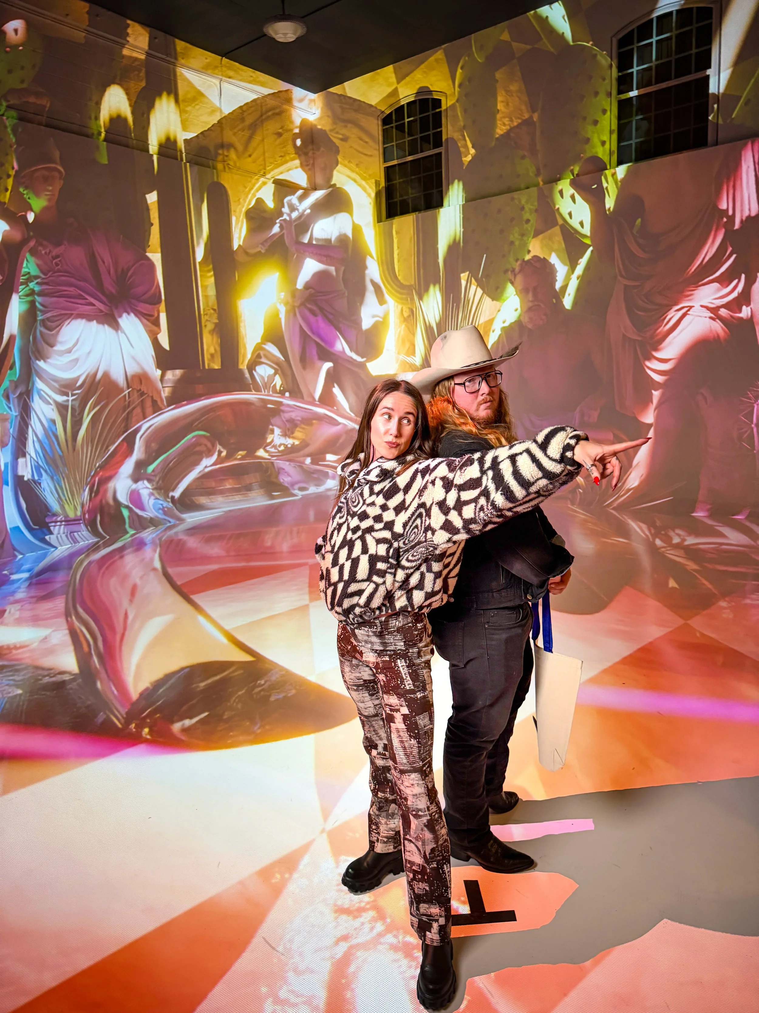 Immersive projection mapping room in swirling chrome and coral visuals, two guests posing as one points across the glowing wall