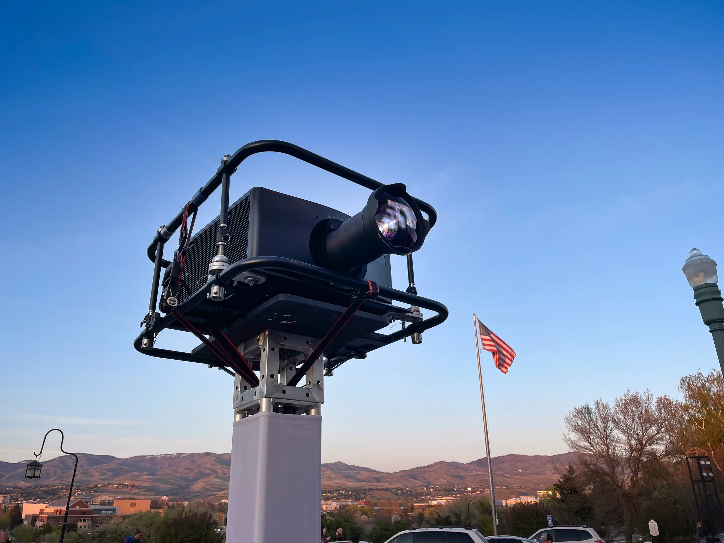Boise Depot projection mapping, laser projector mounted on a tower with foothills and flag behind