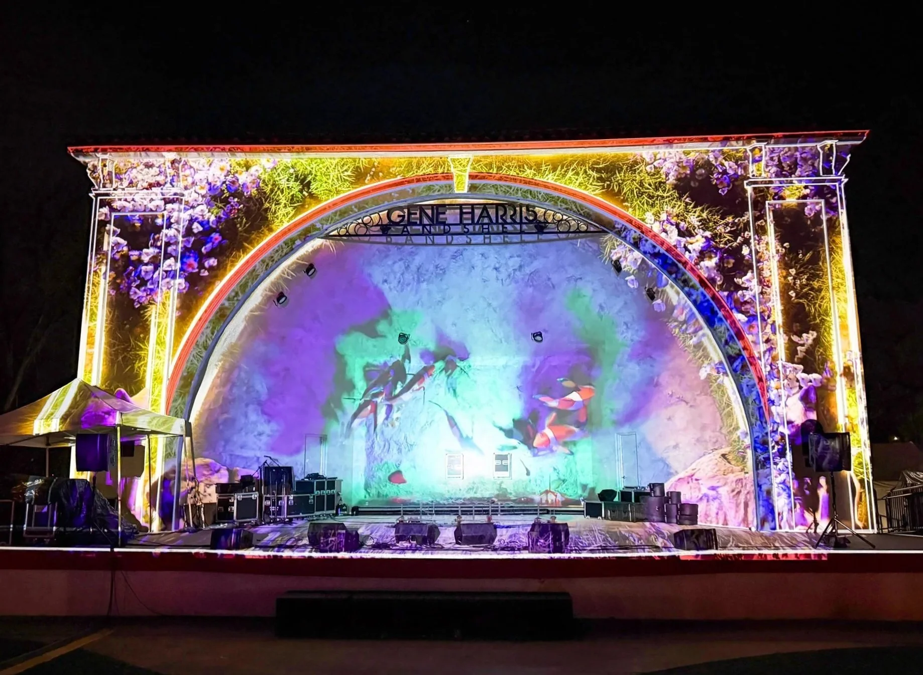Architectural projection mapping on the Gene Harris Band Shell, koi and light filling the arched stage shell at night.