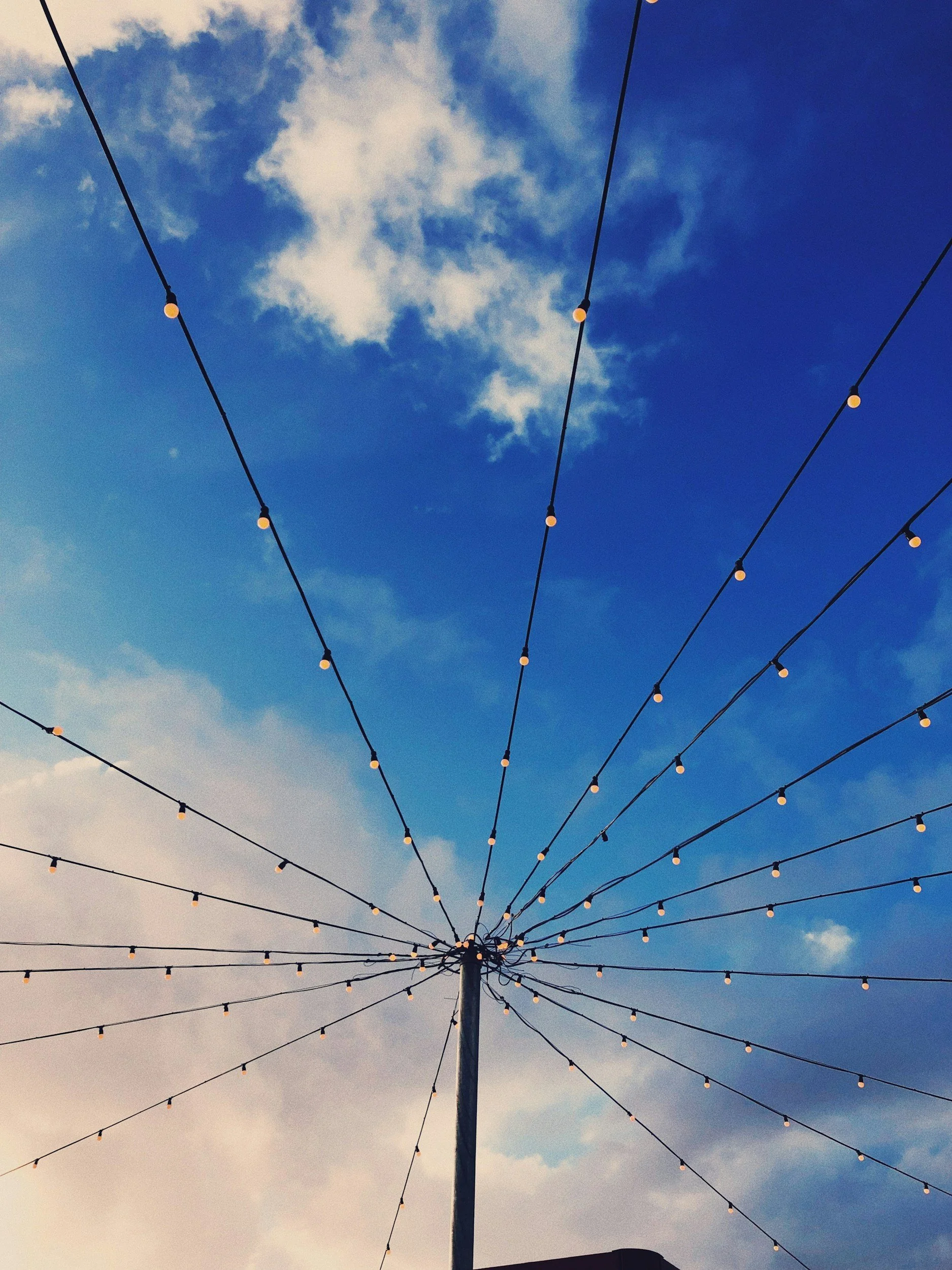String of string lights hanging against a partly cloudy sky at dusk or evening.