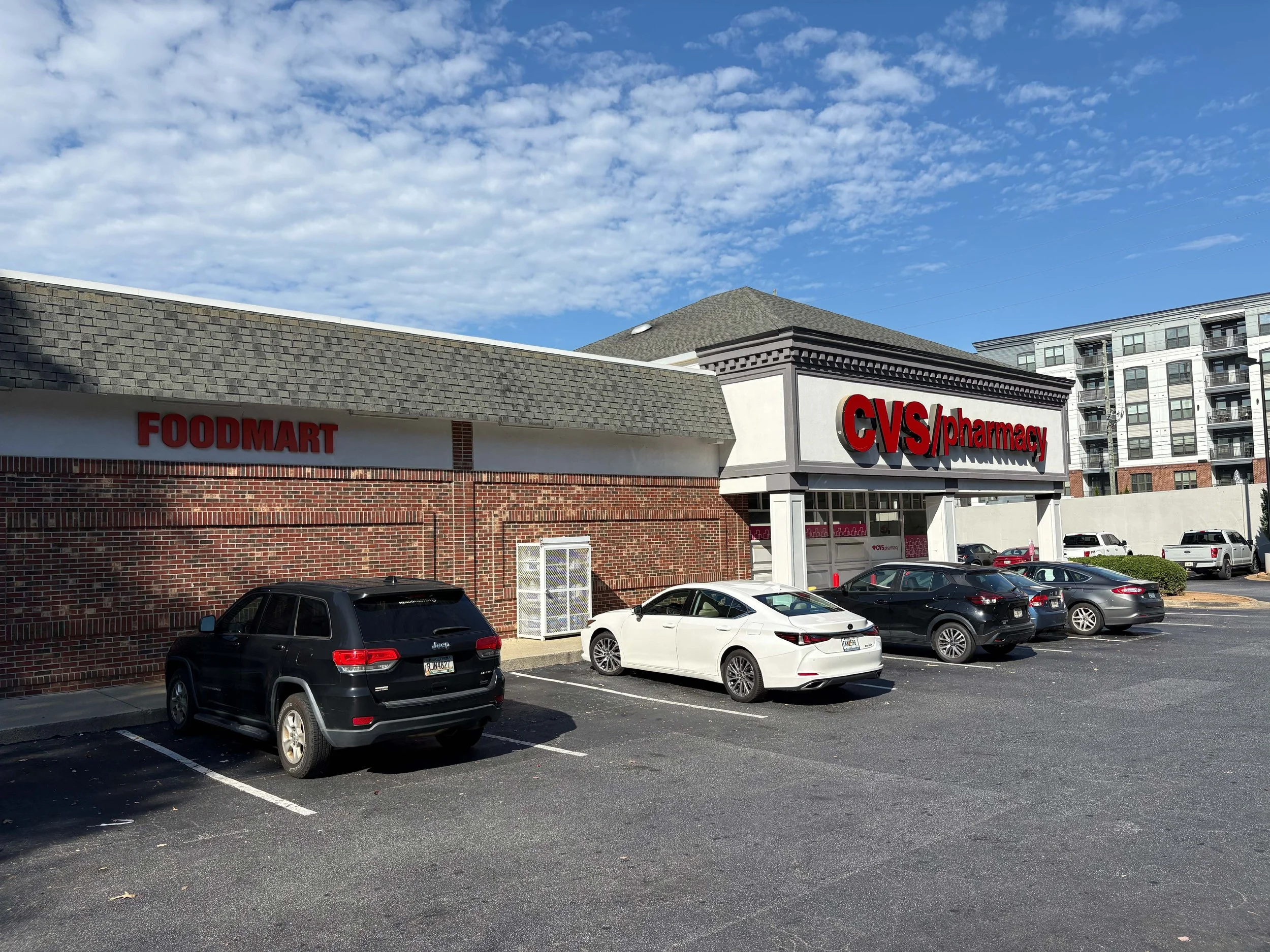 Parking lot in front of CVS pharmacy store with several parked cars and a Food Mart nearby, under a partly cloudy sky.