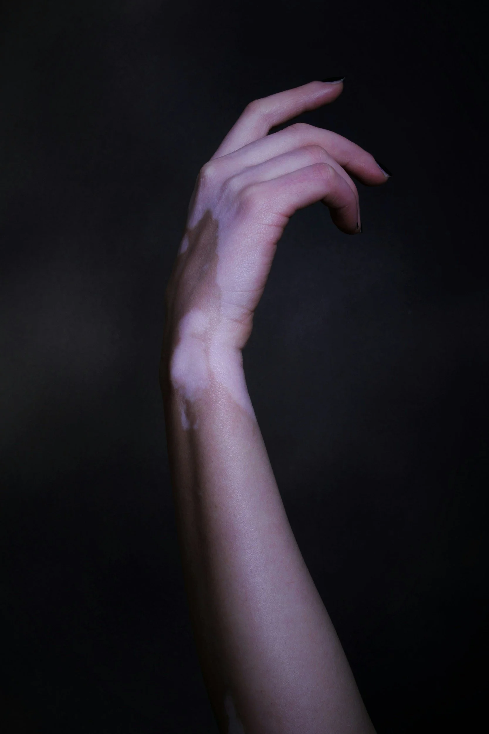 A hand with black nail polish on a dark background, fingers elegantly curved.
