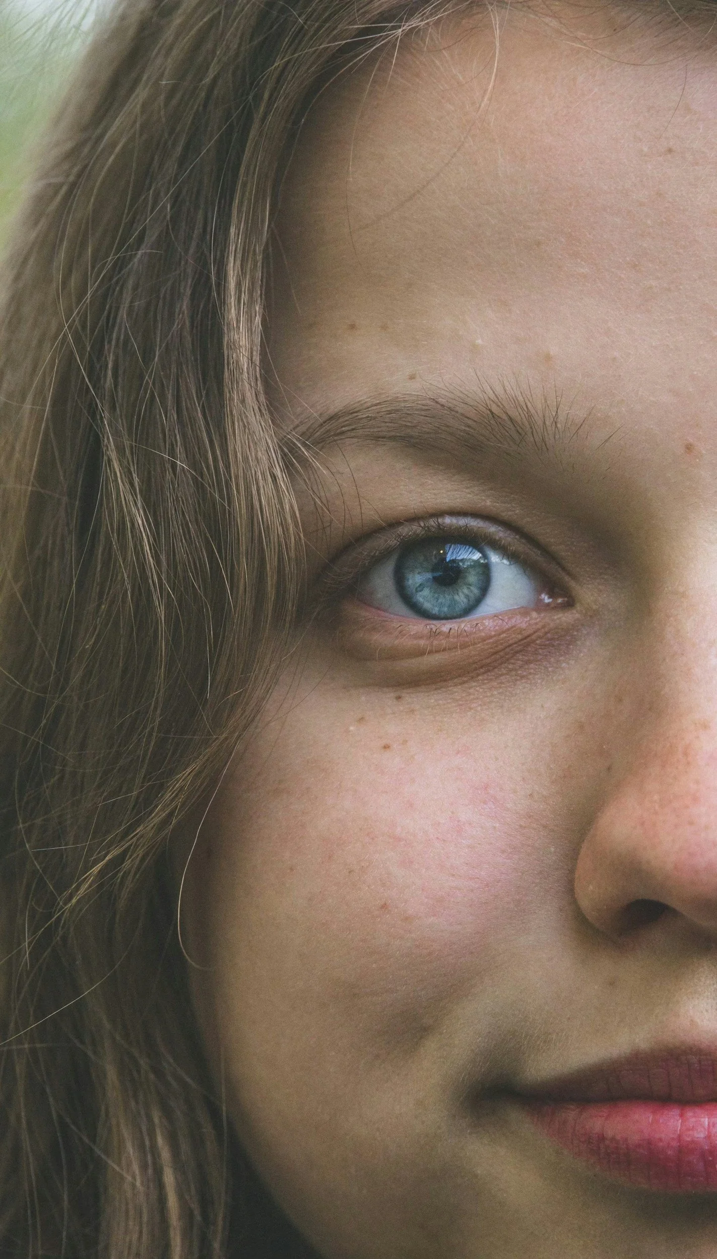 Close-up of a woman's face showing her blue eye, part of her nose, and lips, with light skin and long brown hair.