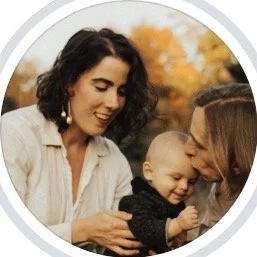 A woman, a man,  and a baby outdoors during fall, smiling and engaging with the baby.