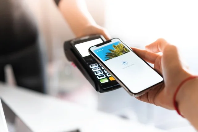 Person paying with a smartphone using contactless payment at a point of sale device.