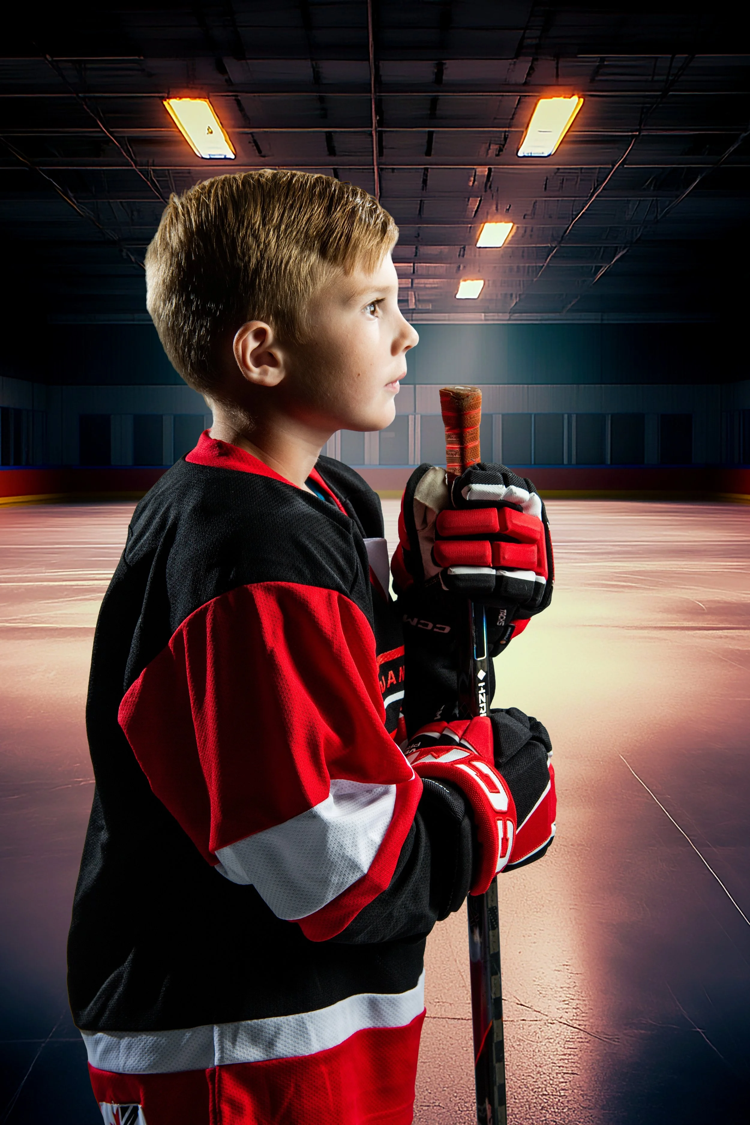 Profile of a young boy in a hockey jersey holding a hockey stick inside an ice rink.