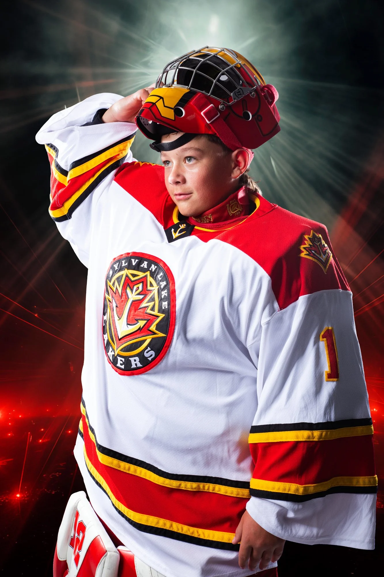 Young hockey player in a red, white, and yellow uniform with a team logo, wearing a red helmet, holding the helmet, standing against a dynamic, abstract background with radial light bursts and red highlights.
