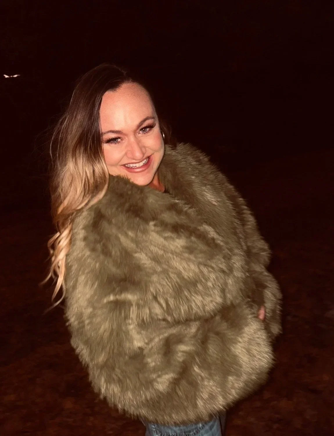 A woman smiling while wearing a large fur coat.