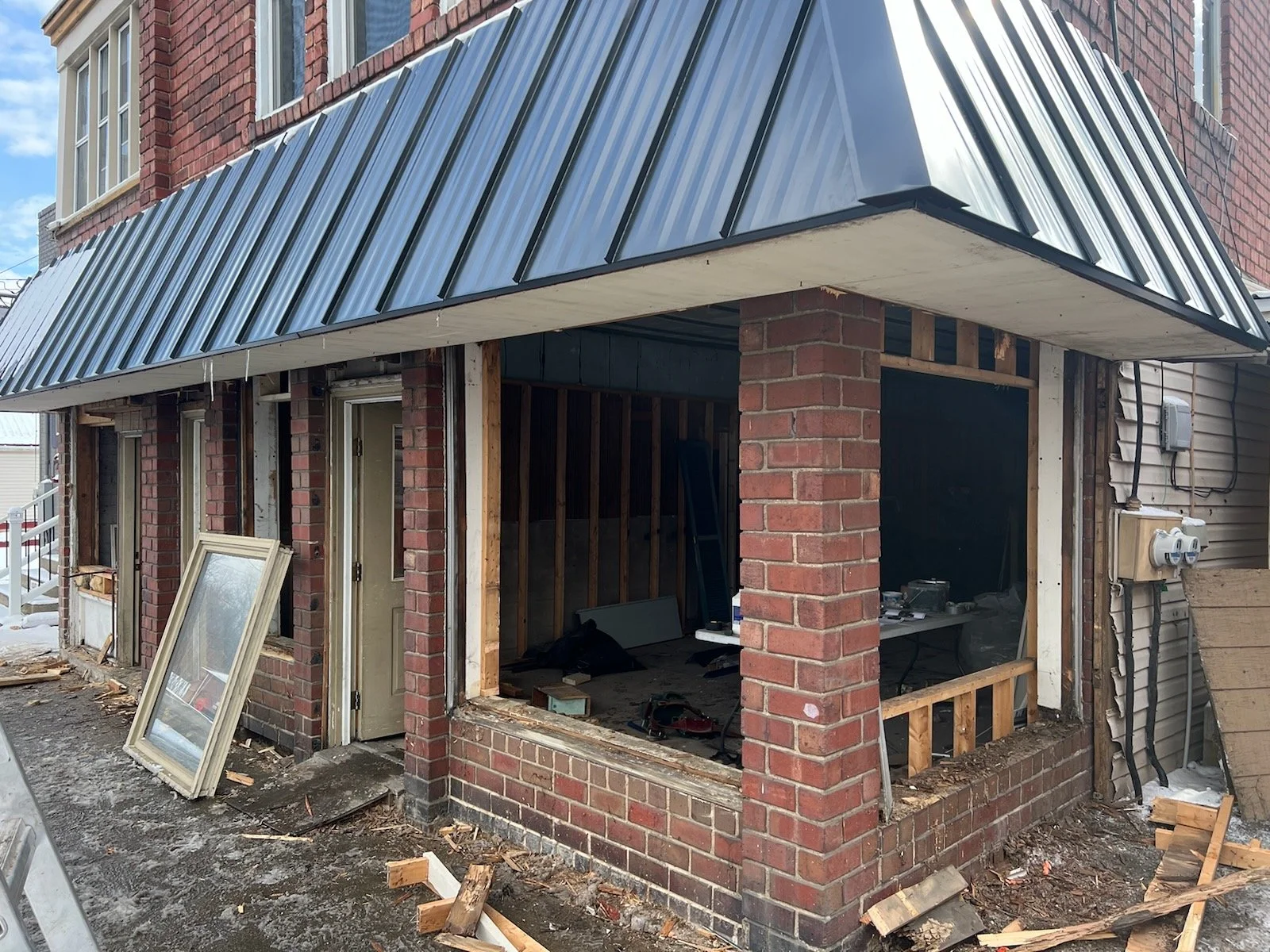 Undergoing renovation, building exterior with brick walls, open window frames, and construction tools on ground.