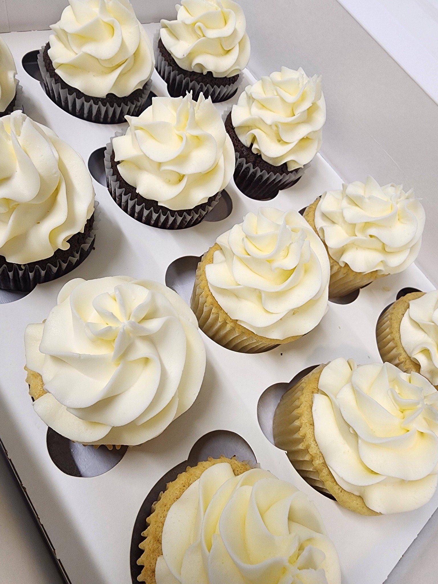 Cupcakes with white frosting in black and white liners arranged in a box.