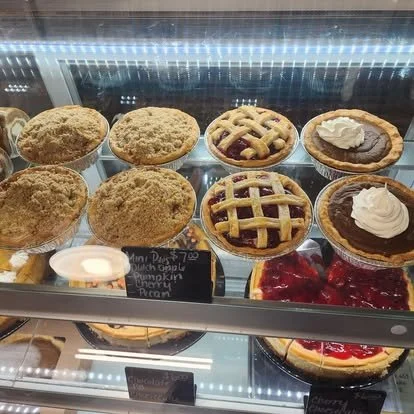 Display case with various pies and baked goods, including apple, pumpkin, cherry, and chocolate pies, some topped with whipped cream.
