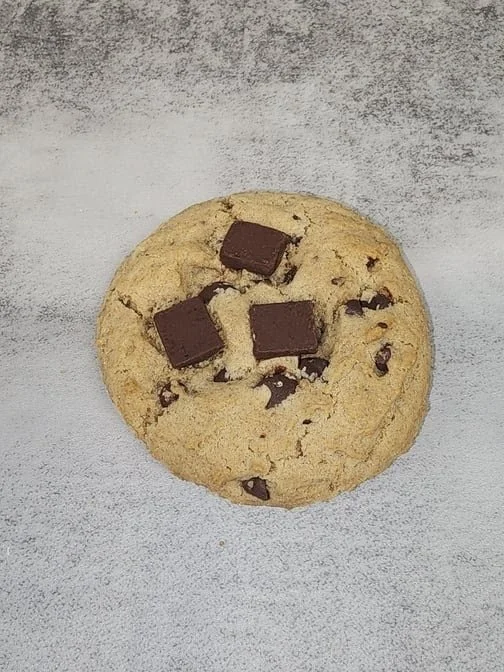 A chocolate chip cookie with four pieces of chocolate on top, placed on a gray textured surface.