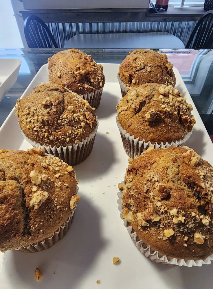 Six muffins with crumbly topping on a white tray.