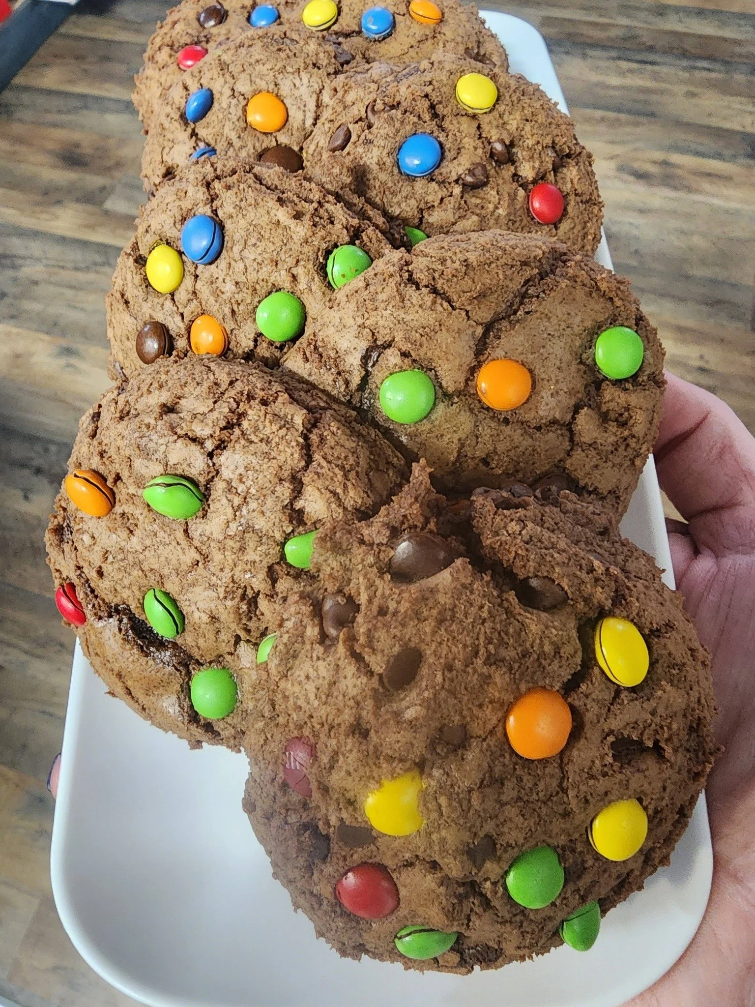 Four large chocolate cookies with colorful candy-coated chocolates on top, served on a white rectangular plate.
