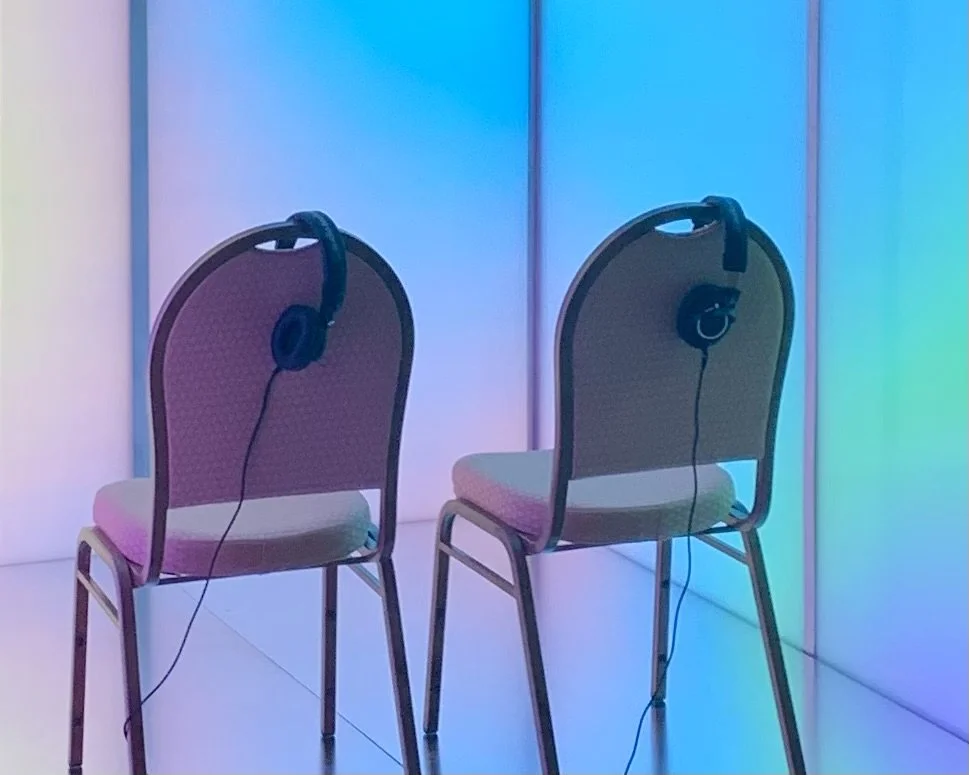 Two chairs inside mood elevator with headphones placed on the back of each chair in front of a "Laura" a colorful multi color gradient  during rest cycle of mood elevator.