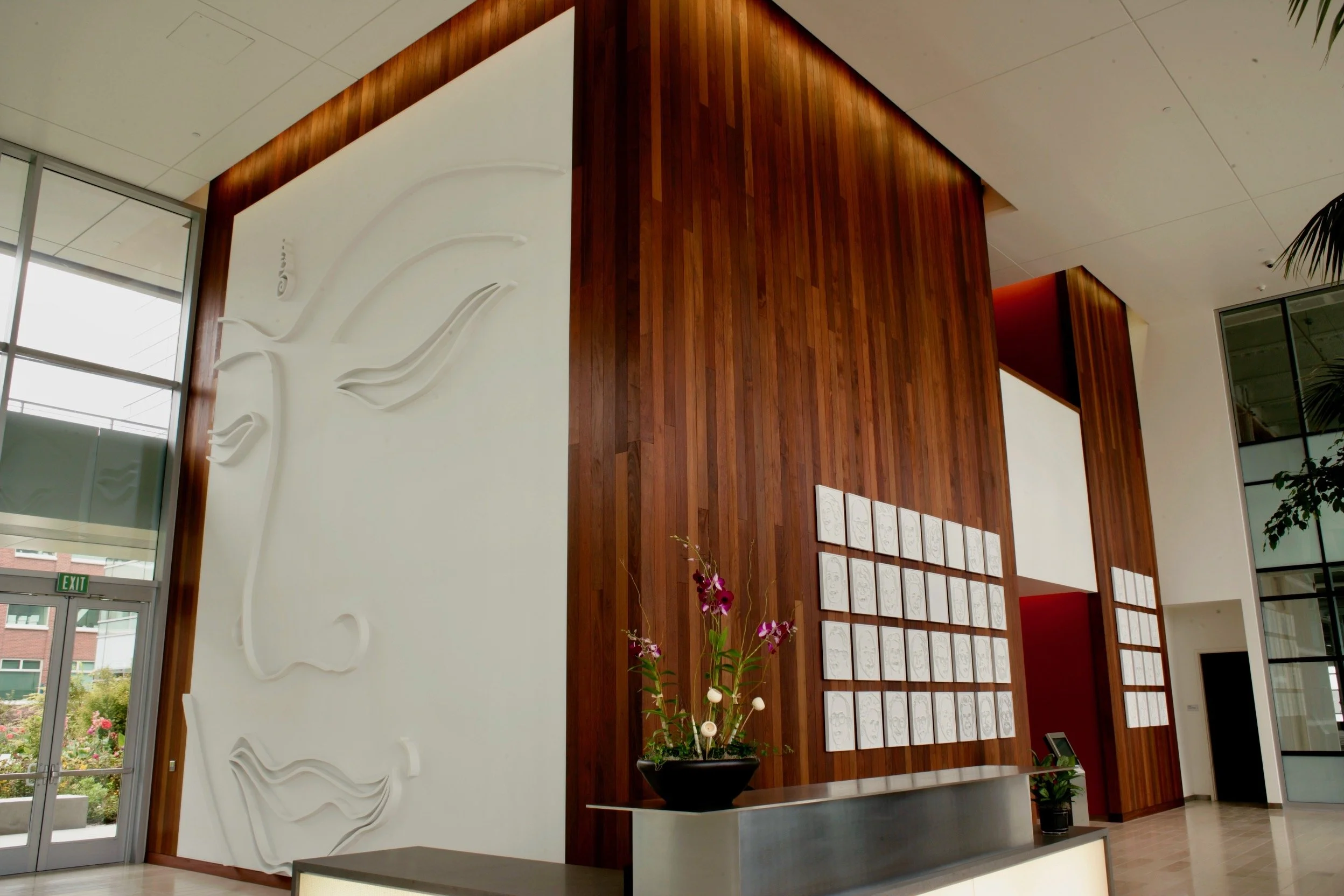 Modern interior lobby with a large white sculpture of Buddha  on a white wall, wooden paneling, and framed white artworks of all the Nobel prize winning scientists from the Bay area.