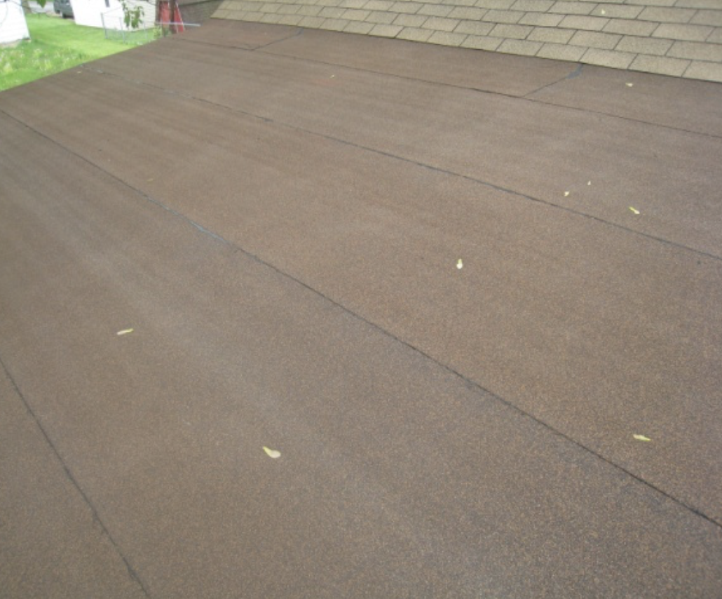 Brown modified bitumen roof with a few small yellow leaves scattered on it.
