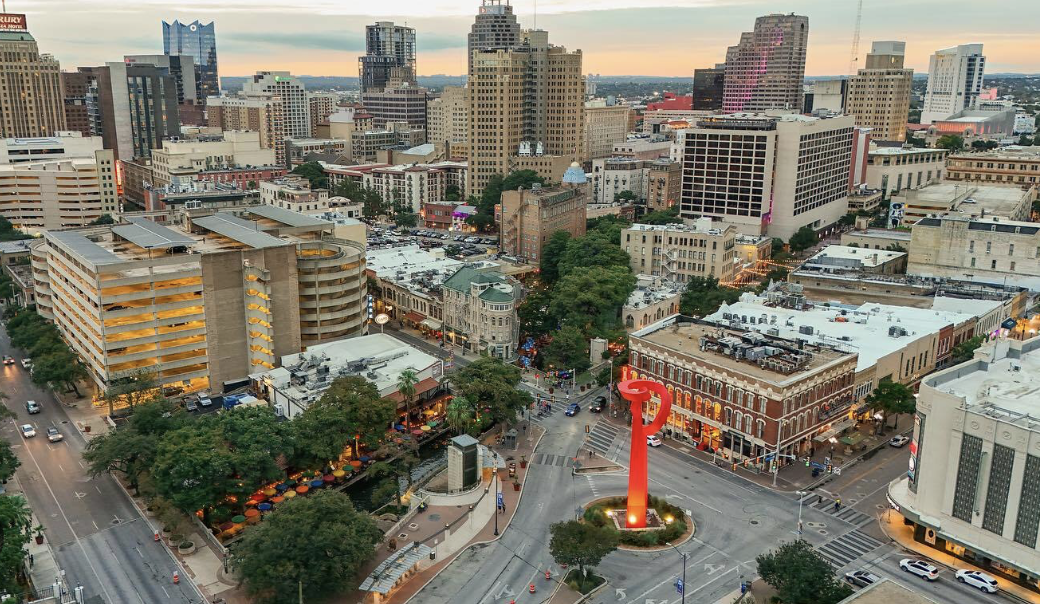 Aerial view of downtown Nashville, Tennessee, showing skyscrapers, historic buildings, a large red musical note sculpture, and bustling streets at sunset.