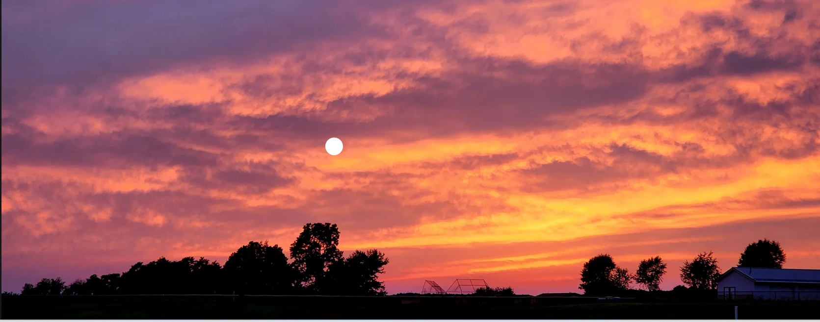 A colorful sunset sky with shades of pink, orange, and purple over a silhouette of trees, a house, and playing field equipment.