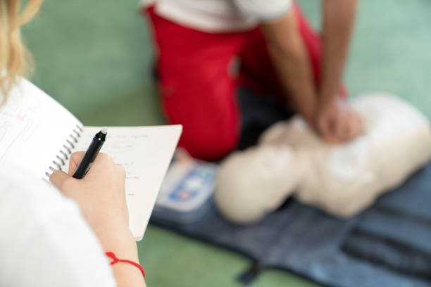 Healthcare professional taking notes during CPR training on a mannequin.