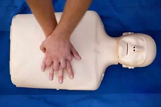 Person practicing CPR on a dummy chest with a head, on a blue surface.