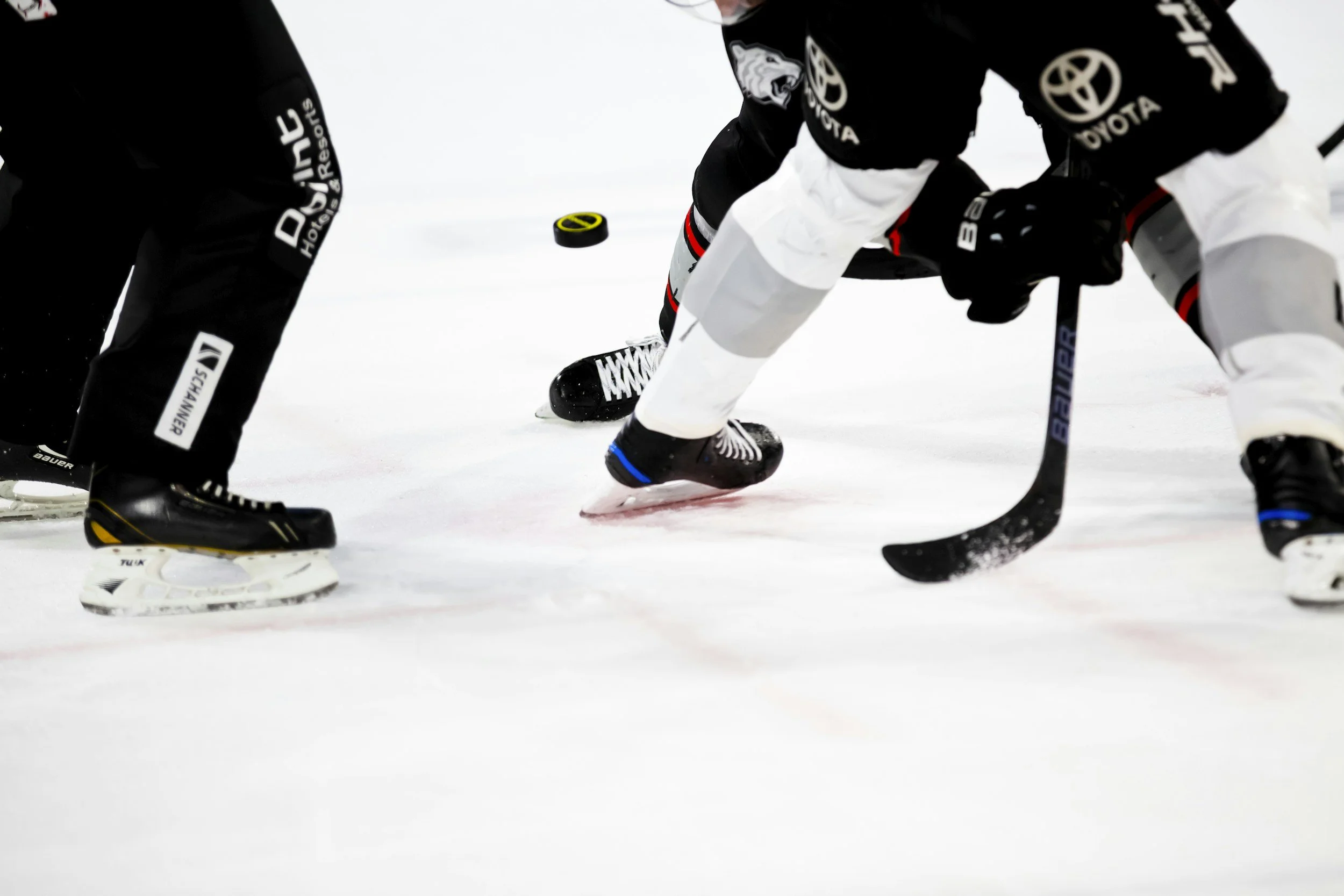 Hockey players engaged in a game on the ice, focusing on their skates, sticks, and puck.