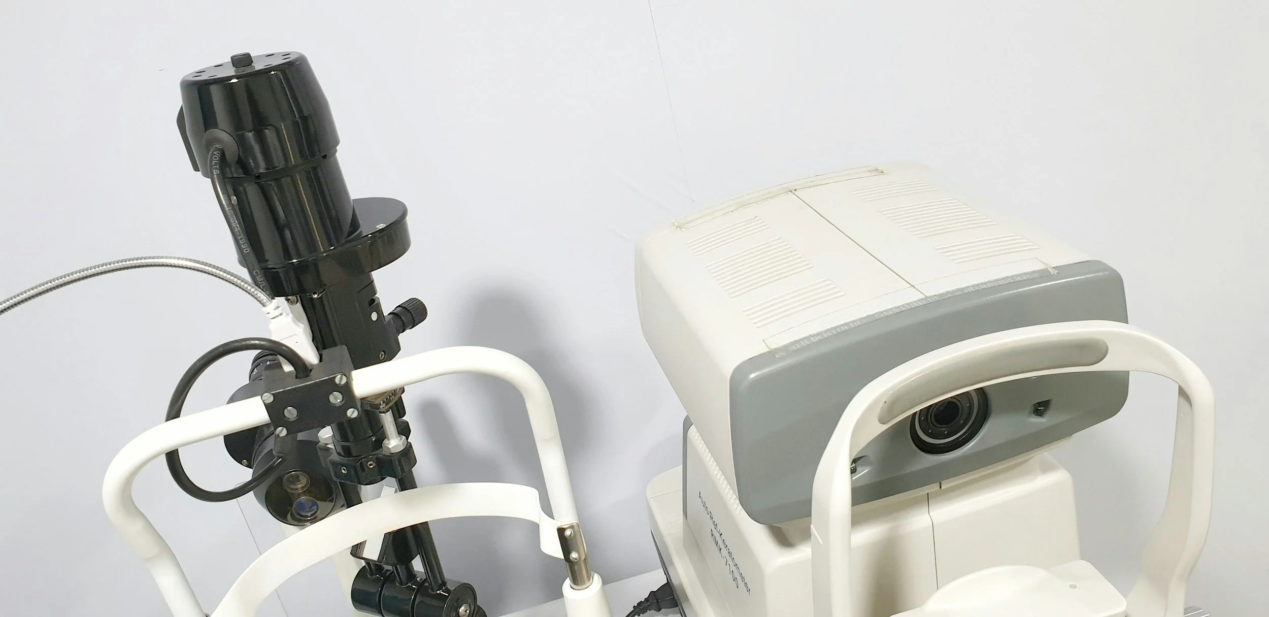 Medical equipment including a black ophthalmic device and a white scanning or imaging machine in a clinical setting.
