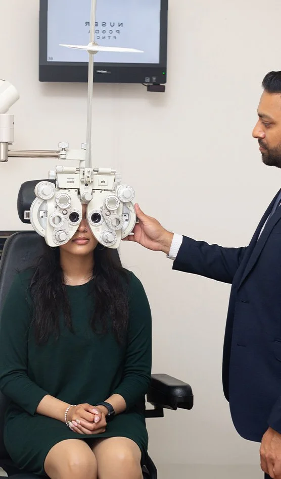 Optometrist performing eye exam on woman with phoropter in an eye clinic.