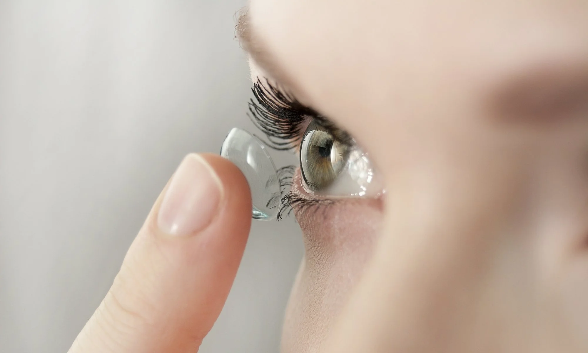 Close-up of a person inserting a contact lens into their eye with a finger.