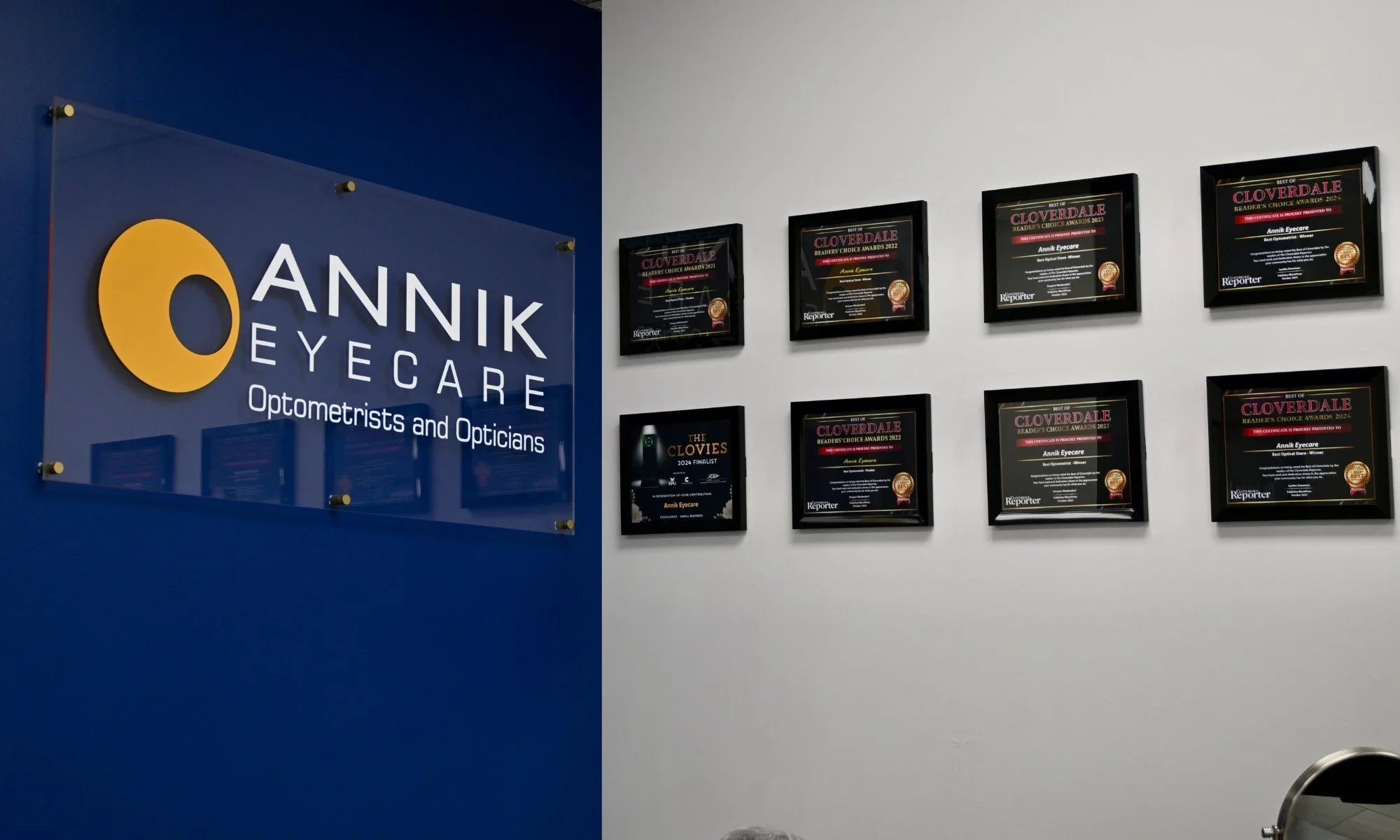 Wall in a doctor's office with a sign for Annik Eyecare, and several award plaques displayed on the wall.