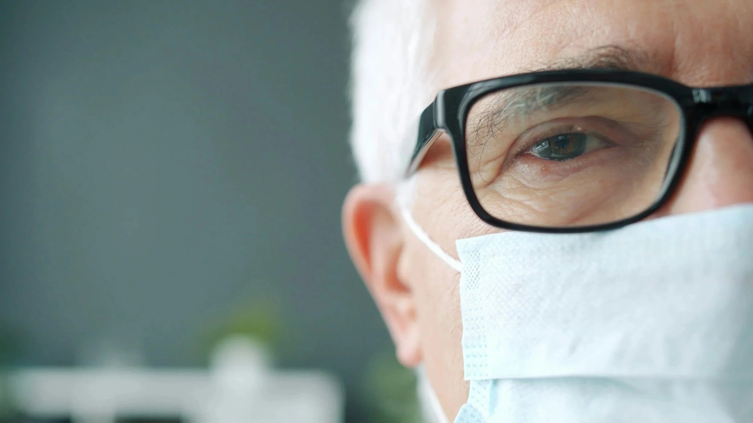 Close-up of a person's face wearing glasses and a face mask, focusing on their eye.
