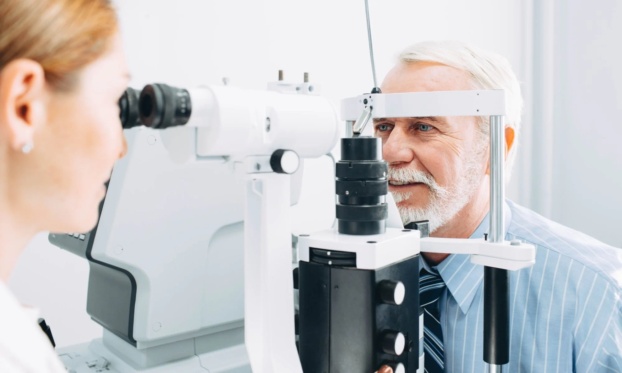 Optometrist conducting eye exam on an elderly male patient using slit lamp