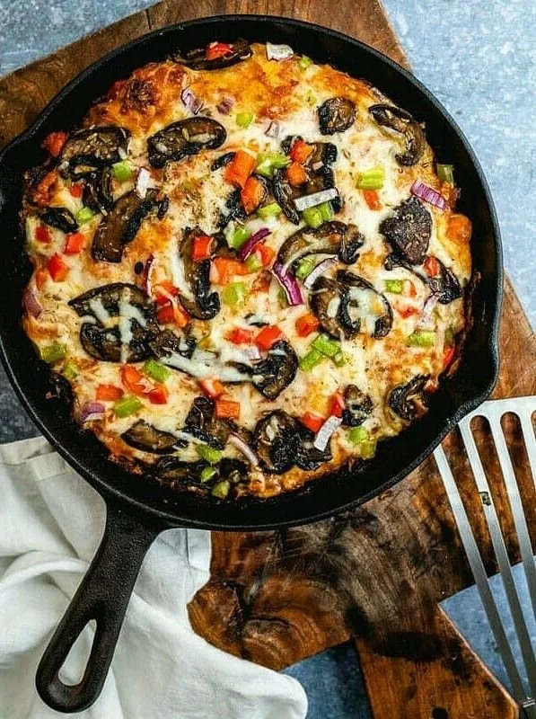 A homemade pizza in a cast iron skillet topped with melted cheese, sliced black olives, diced red and green bell peppers, and red onions.