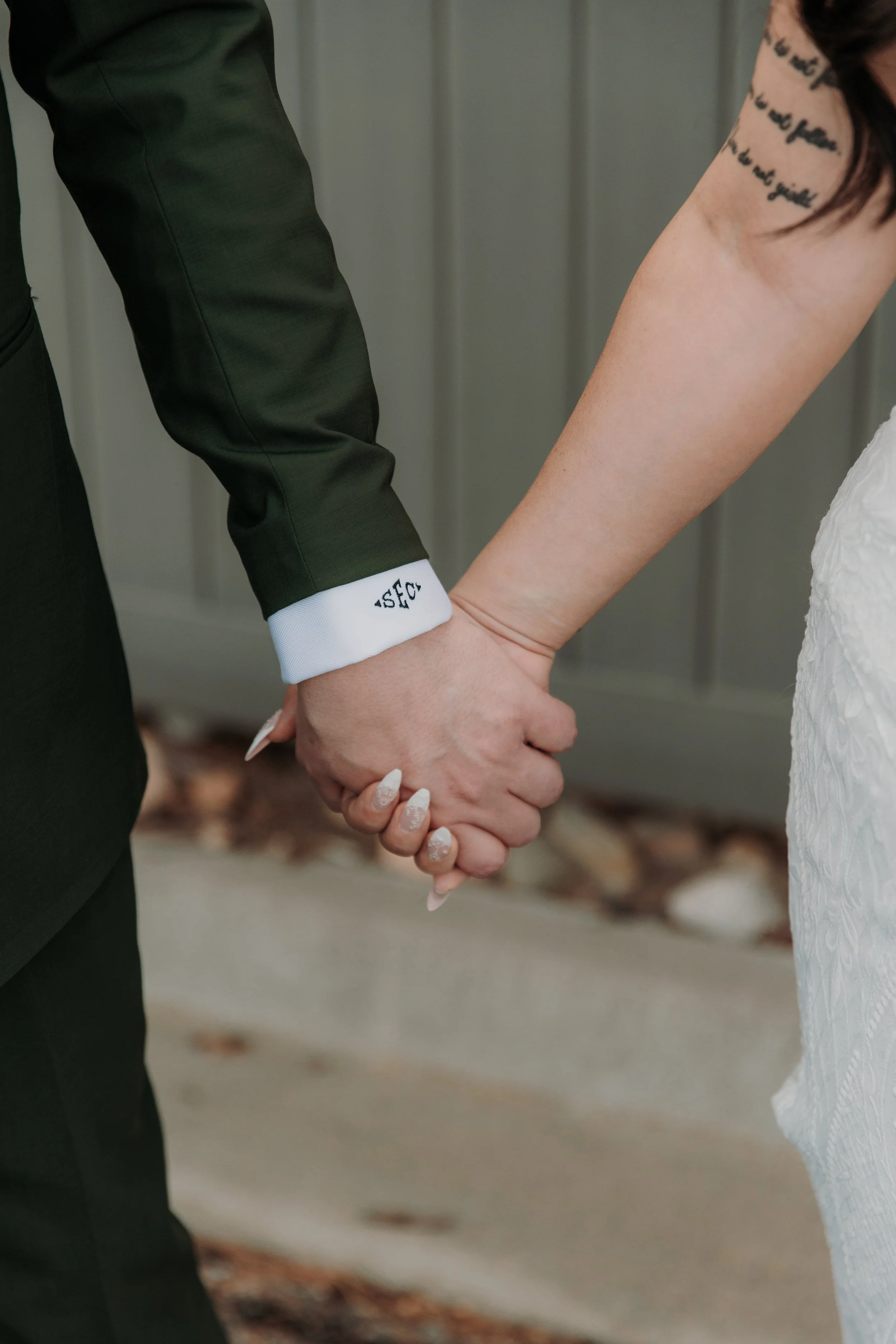 Close-up of a bride and groom holding hands during a wedding ceremony, with the groom wearing a dark suit and the bride in a white dress.