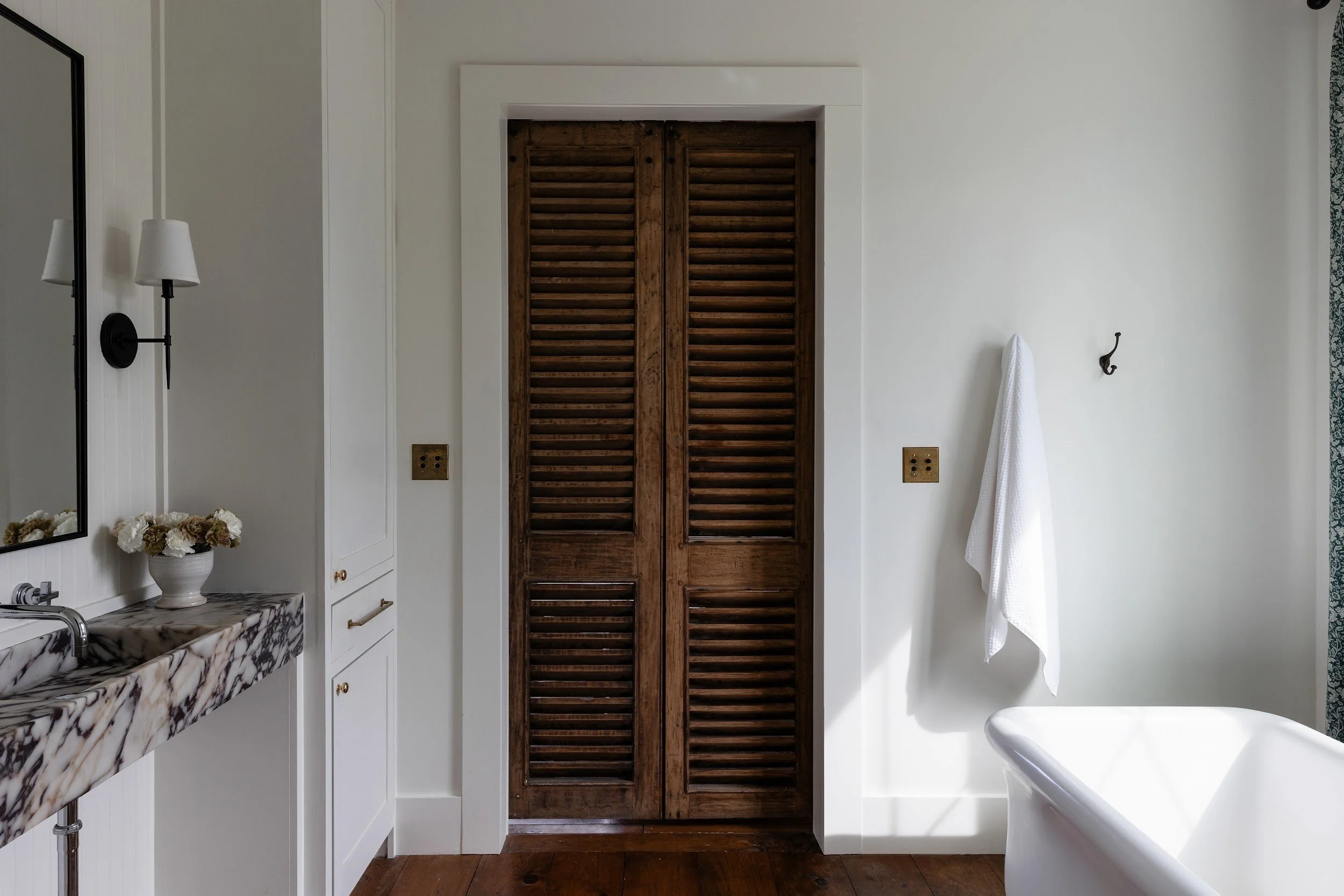 Primary bathroom with marble vanity, freestanding tub and wood doors at Blackbuck Ridge, a custom home in Lampasas, Texas, by Myer & Co. Signature Homes