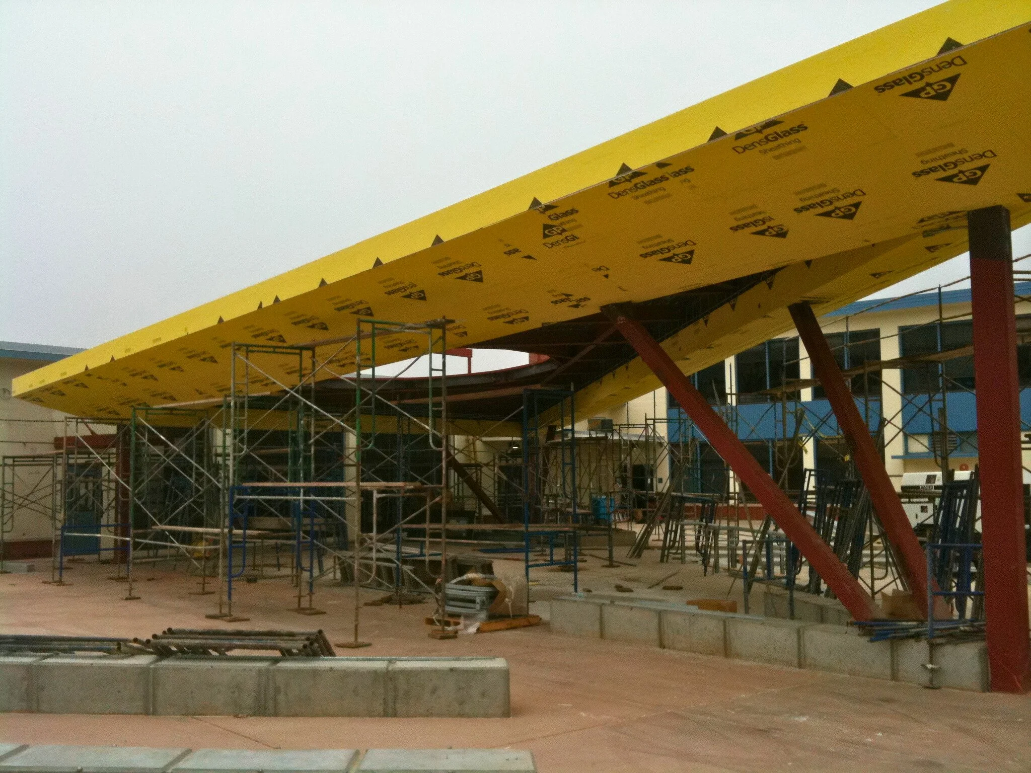 Construction site with scaffolding and a partially built roof structure with yellow insulation panels.