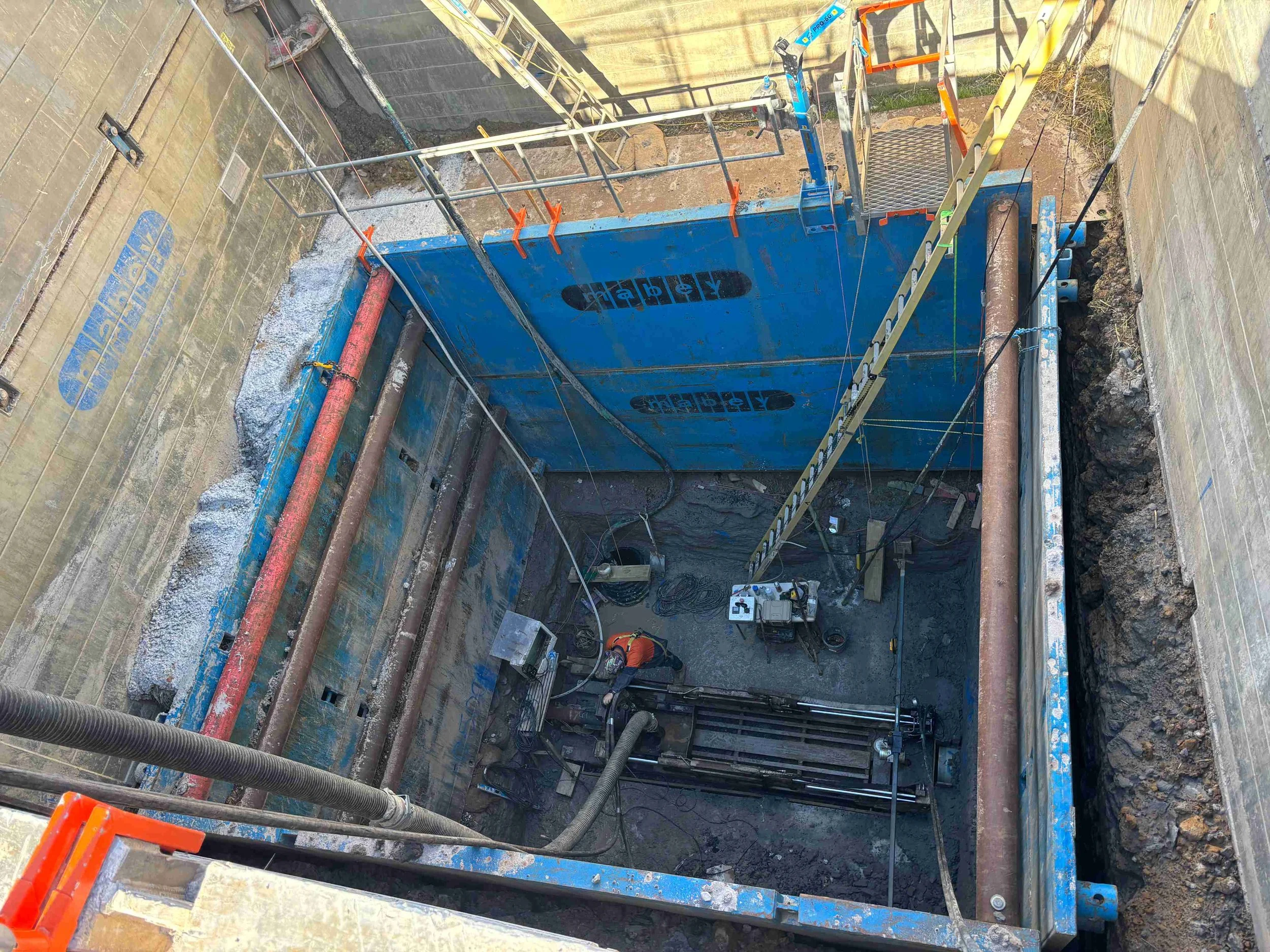 An open bore drilling construction site foundation with excavation equipment, metal piping, safety barriers, and construction tools.