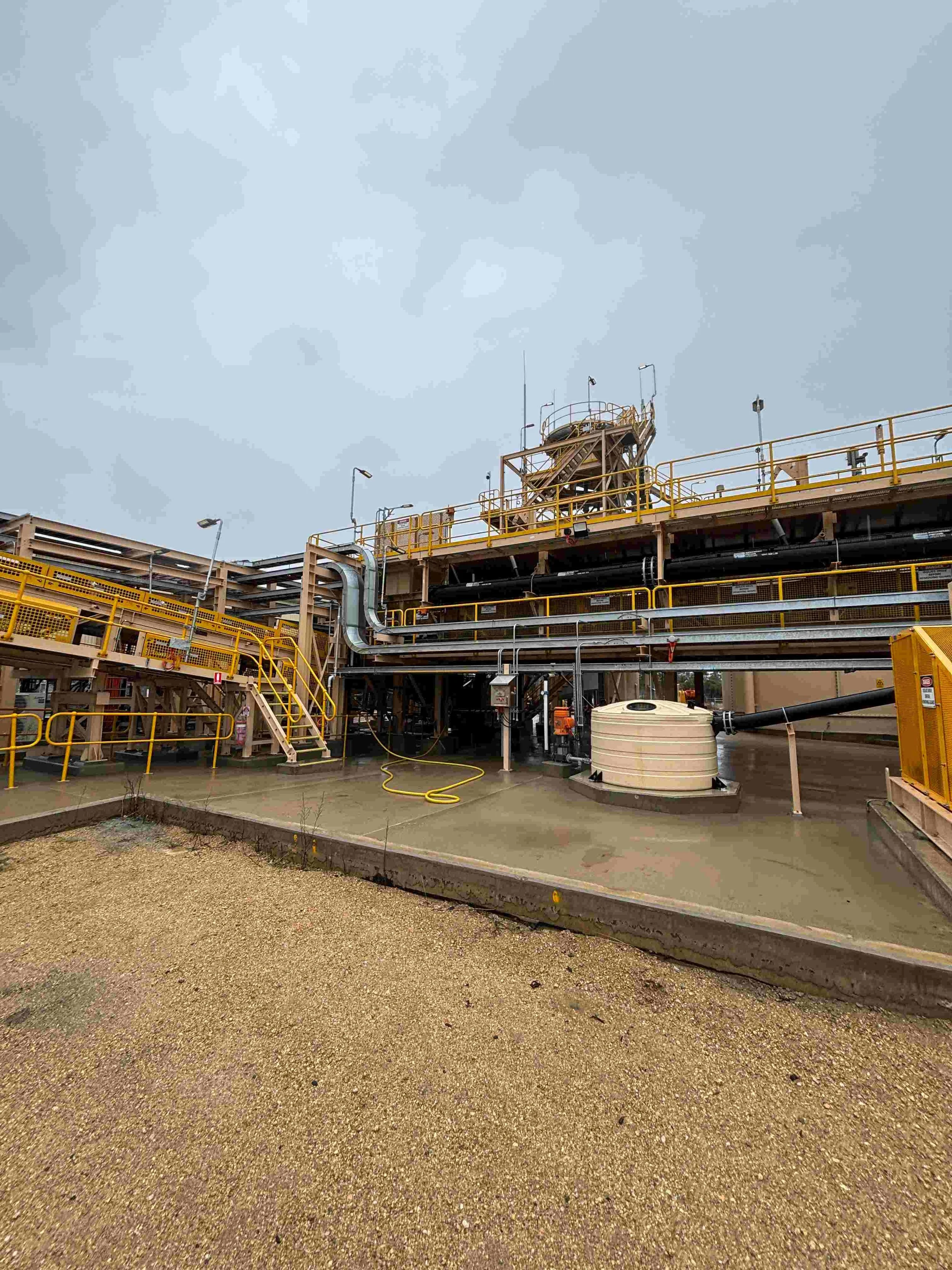 Tomingley with yellow safety railings, stairs, and pipes, and a cloudy sky overhead.