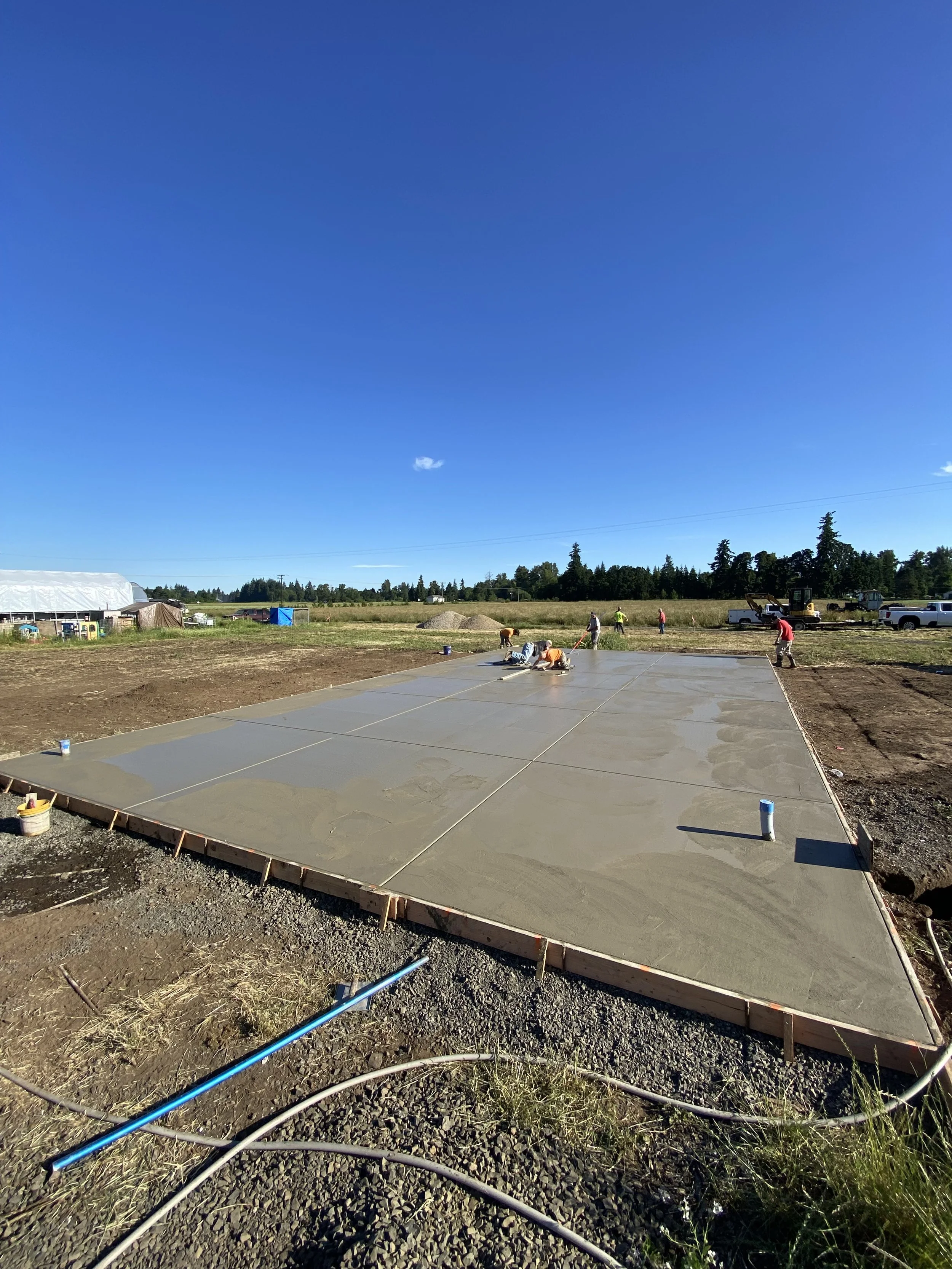 Workers laying down a concrete slab foundation outdoors under a clear blue sky.